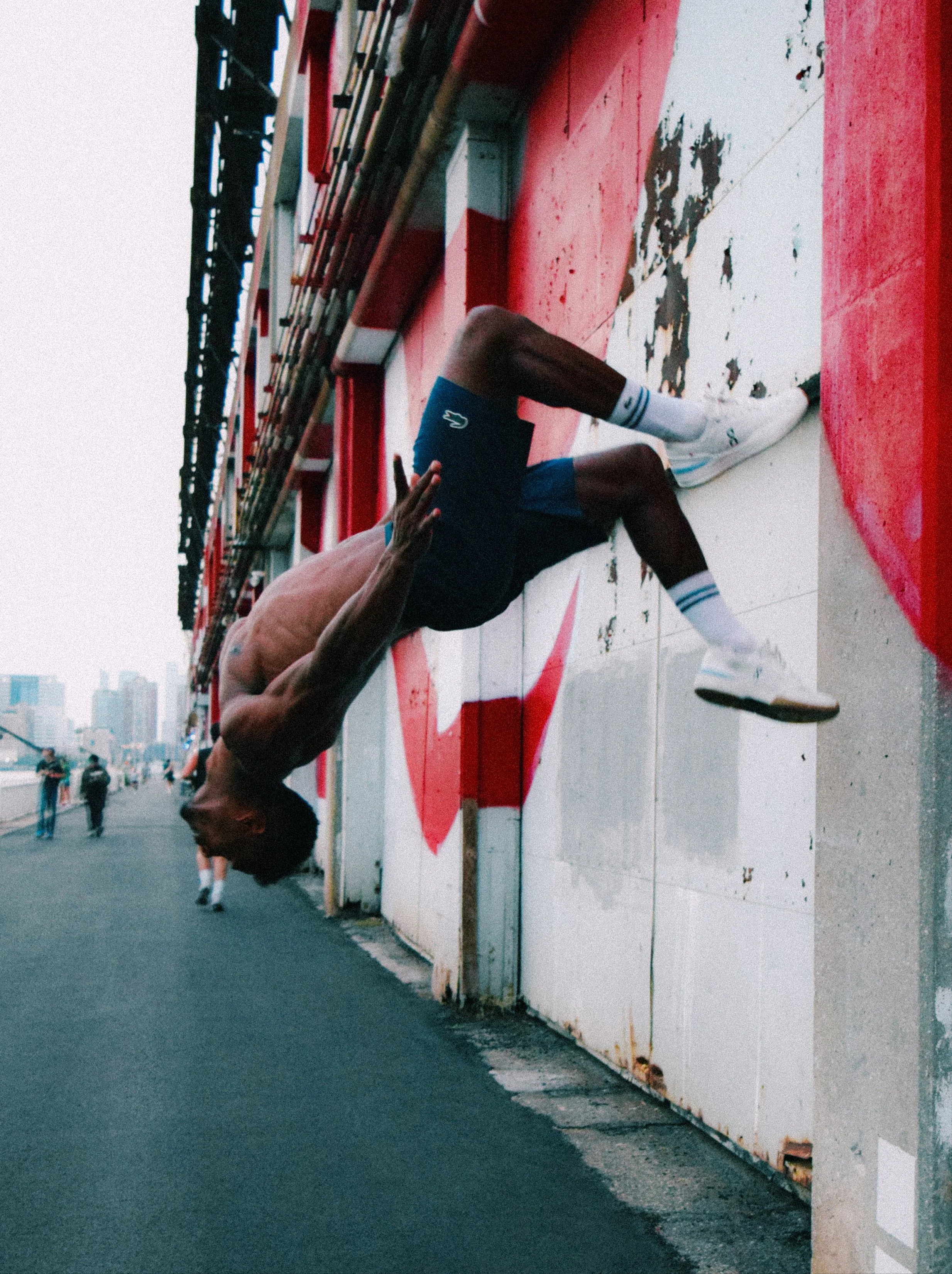 L’un des frères Bertimon saute près d’un mur couvert de graffitis rouges et noirs, dans une photographie en couleur.