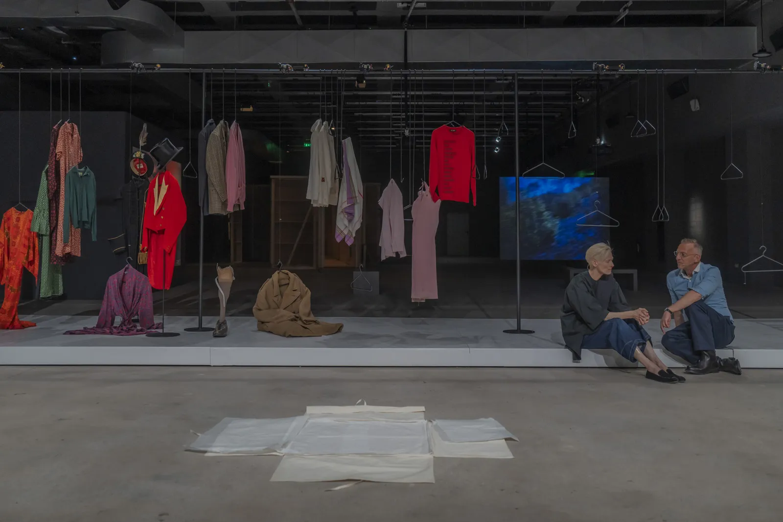 Vue d’ensemble de la performance A Biographical Wardrobe, avec un portant de vêtements colorés installé sur une scène sombre.