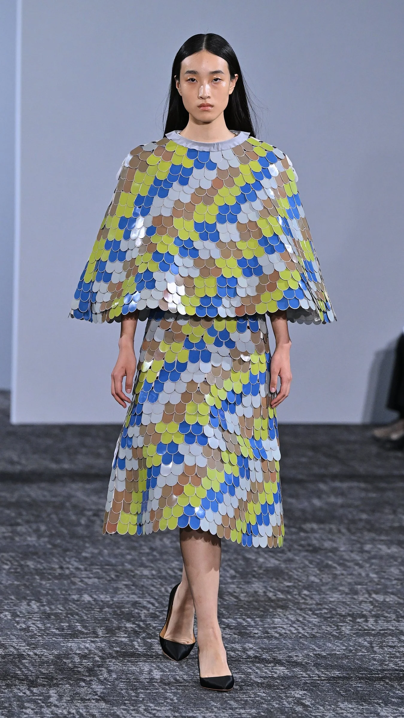 Robe à motifs géométriques jaunes et bleus portée sur le podium du défilé Anrealage printemps-été 2027.