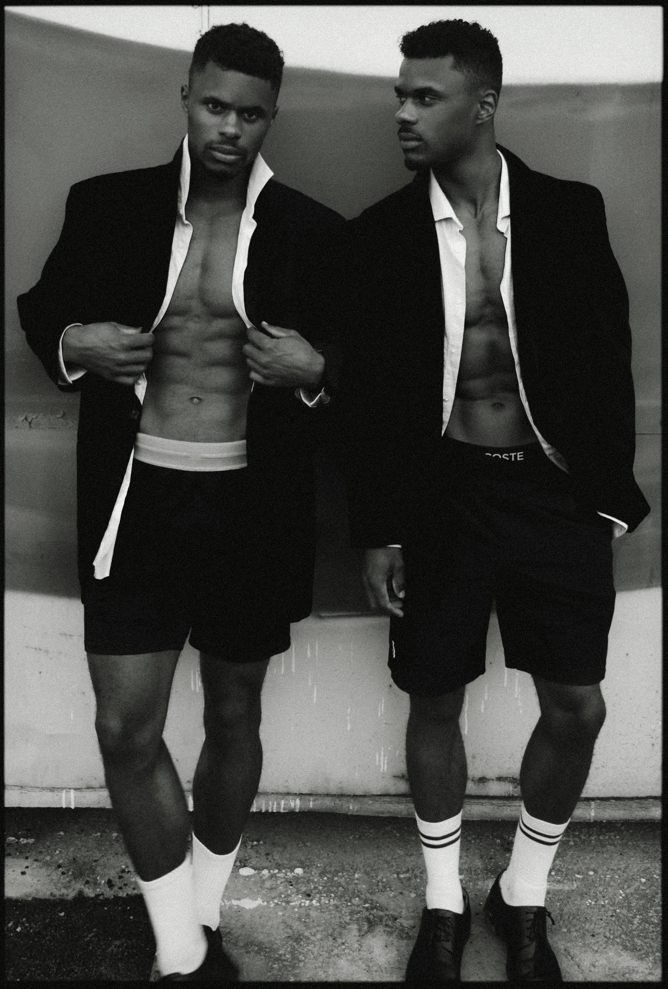 Charles et Maxence Bertimon debout côte à côte en vestes sombres, shorts, chaussettes claires et chaussures foncées, en noir et blanc.