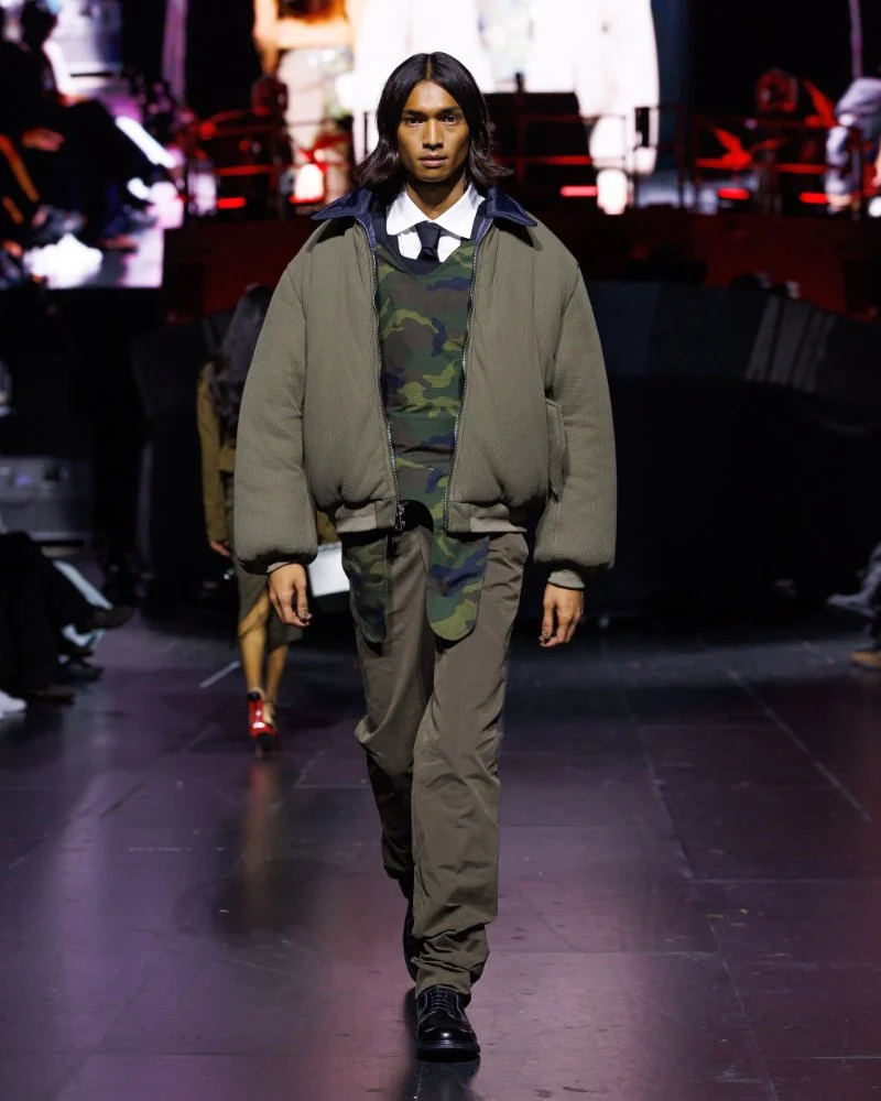Bomber kaki sur un haut camouflage, chemise blanche et cravate, avec pantalon kaki au défilé AWGE SS27.