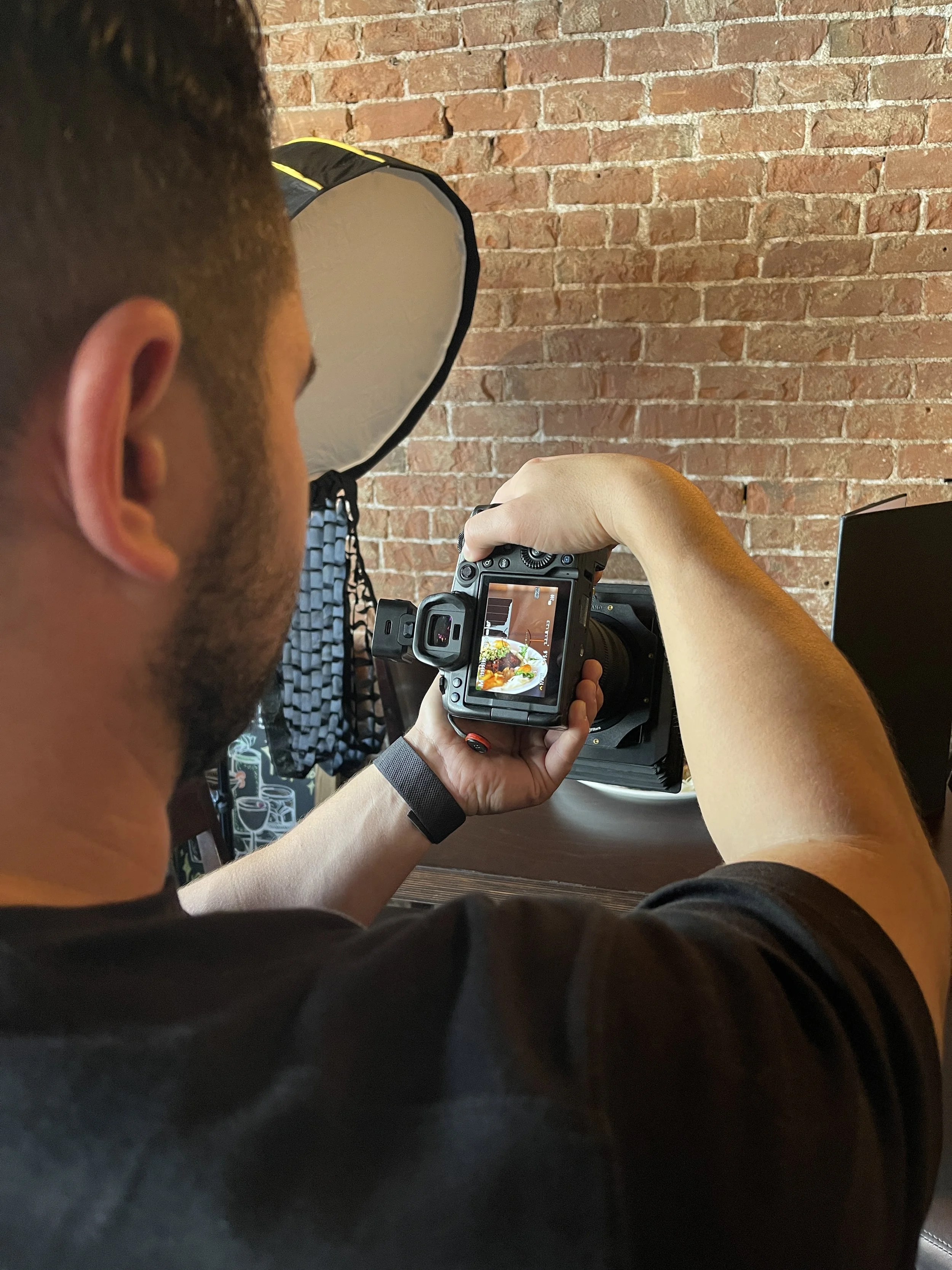 A person with short dark hair holding a camera with a photograph of a dish displayed on its screen.