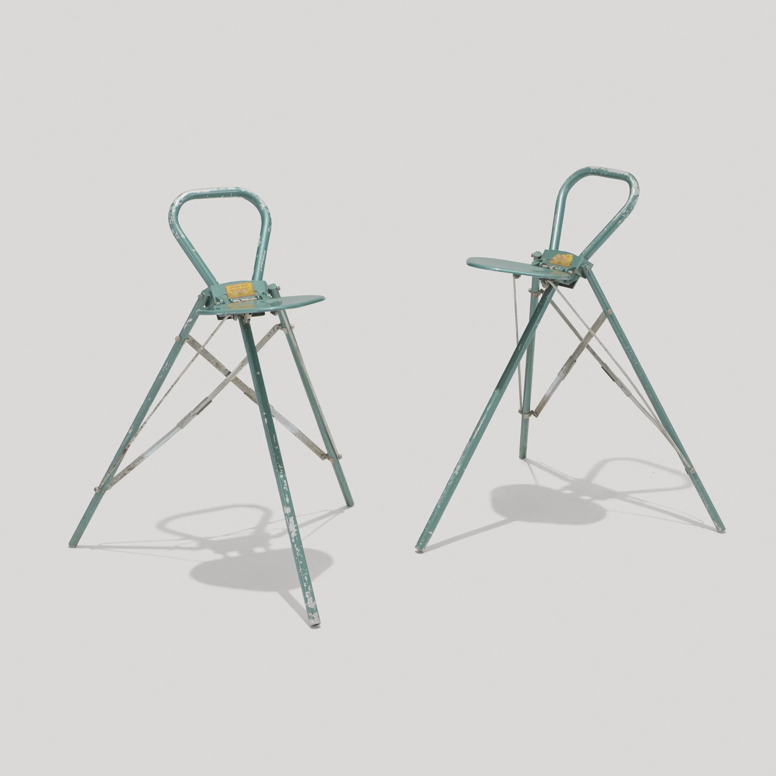 Two worn, teal-colored folding chairs with chipped paint placed on a plain white background.