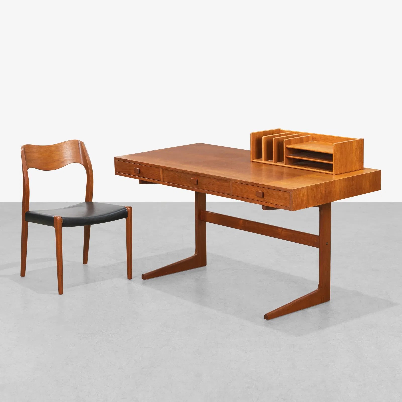 A wooden desk with drawers, a matching wooden chair with a black seat, and a tabletop organizer with multiple compartments, all set against a white background.