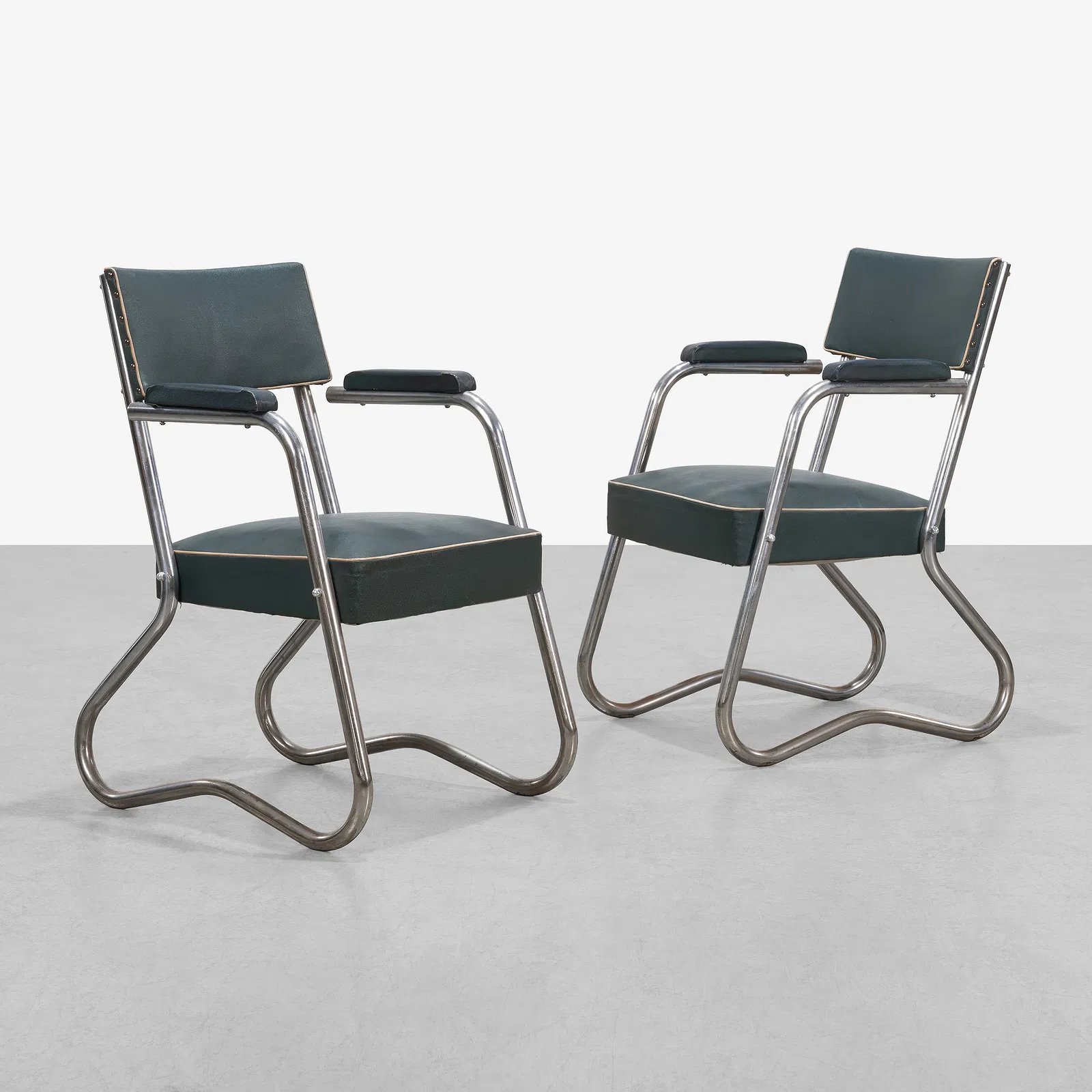 Two vintage chairs with dark green leather seats and backrests, metal frames, and small padded armrests, positioned facing each other against a plain white background.