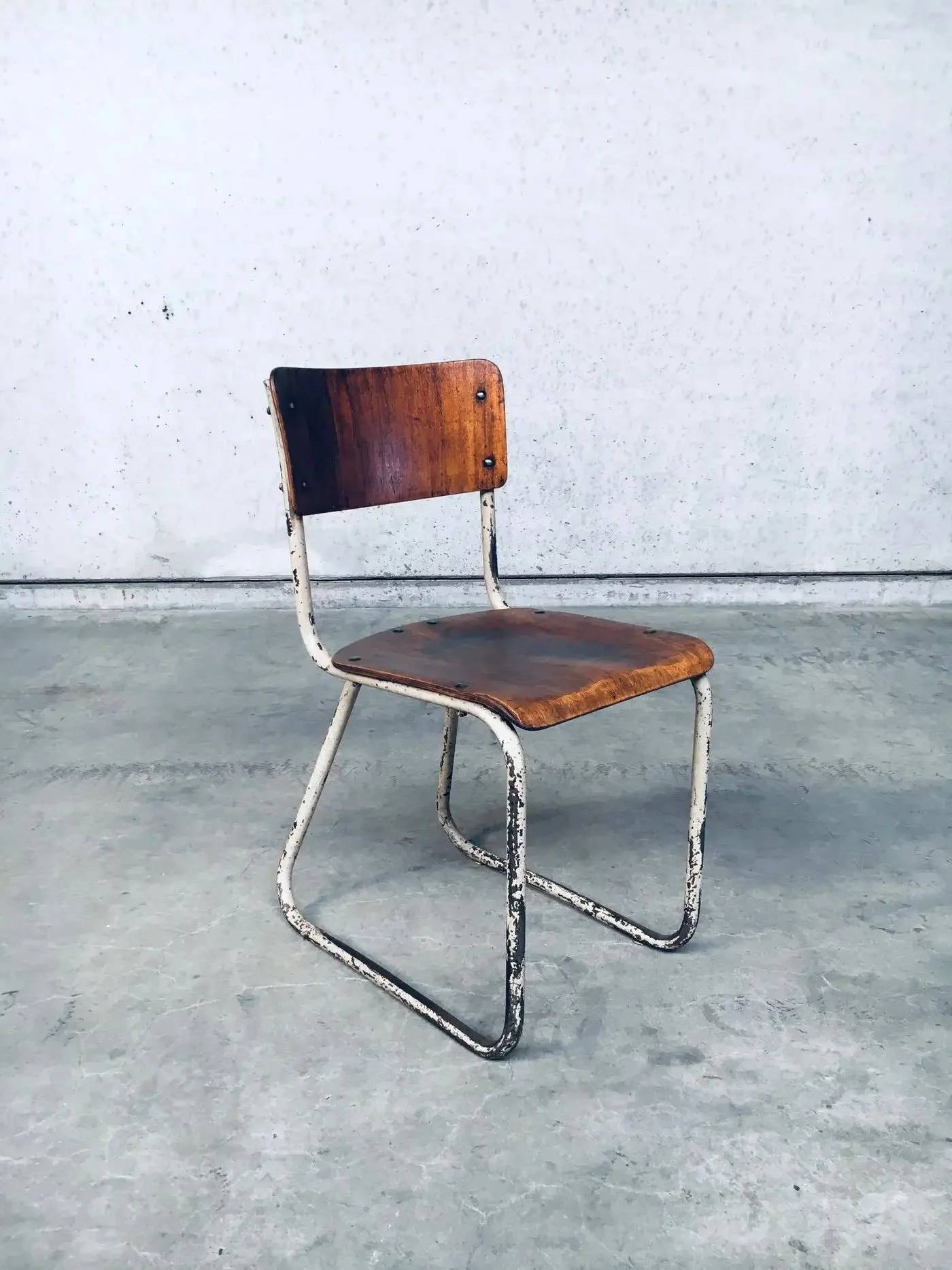 A vintage wooden chair with white metal legs and frame, placed on a concrete floor against a plain white wall.