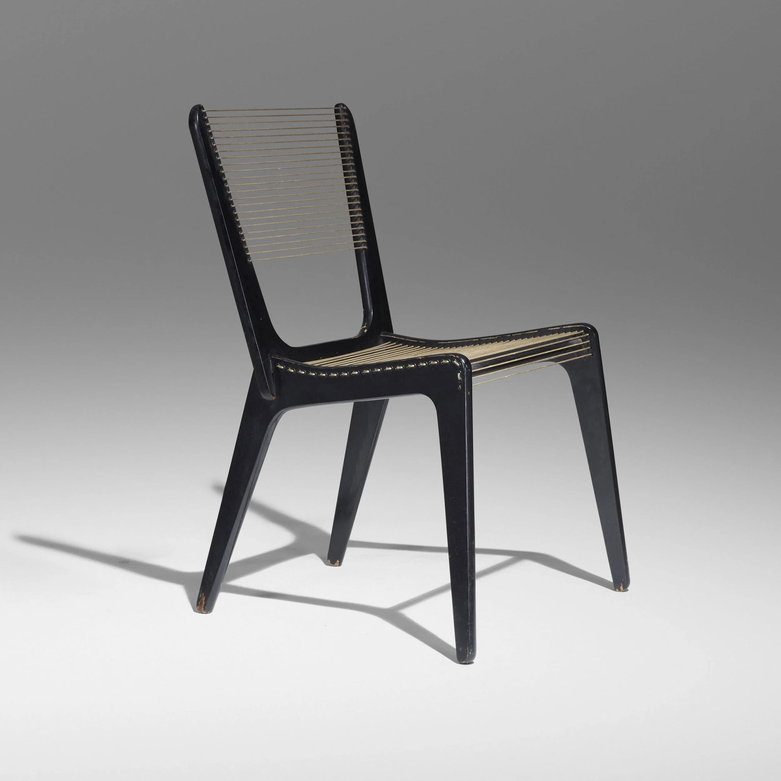 A black chair with a modern design, featuring a frame made of black material with gold accents and thin horizontal metal or plastic slats forming the seat and backrest, set against a plain gray background.