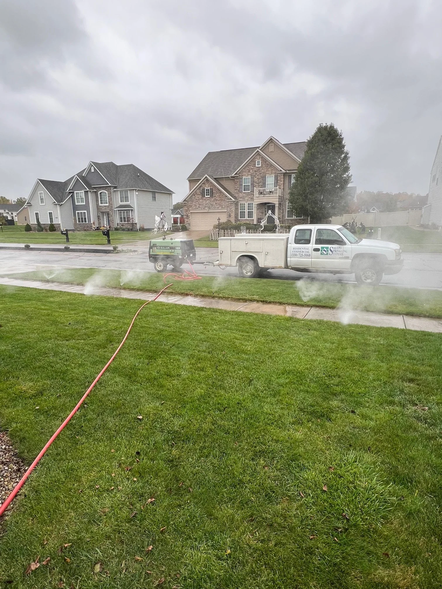 Salupo sprinkler truck is watering the lawn in a neighborhood - expert lawn sprinkling services and maintenance