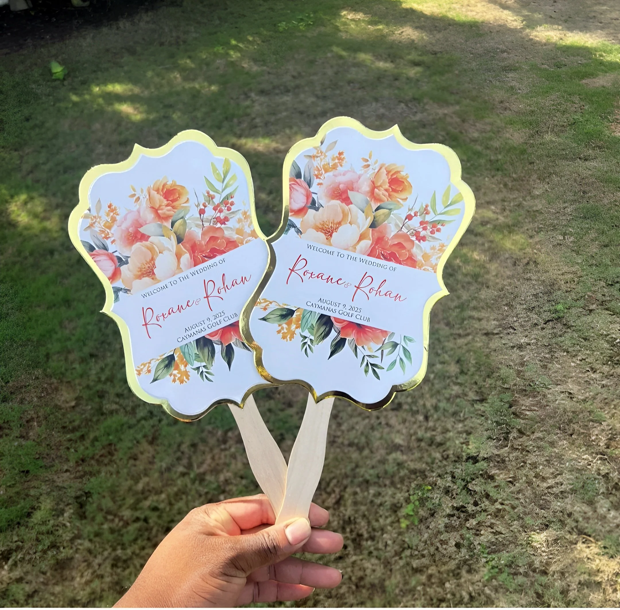 Two decorative signs with floral designs and gold edges, held by a person's hand, welcoming guests to a wedding of Roxane Rohan on August 7, 2025, at Camana's Golf Club.