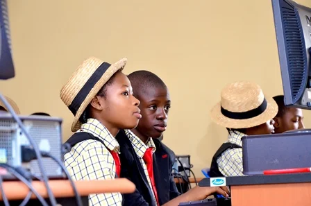 Three students in school uniforms and straw hats sitting at computers in a classroom.