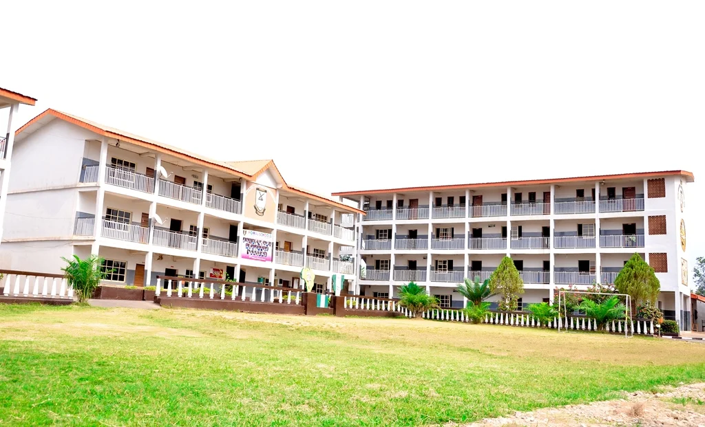Two large, white, multi-story dormitory-style buildings with orange roofs, surrounded by a well-maintained lawn and small palm trees.