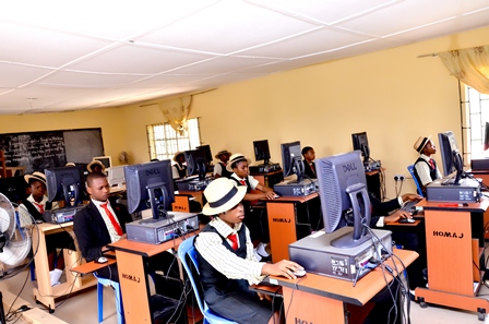 Students in a computer class using desktop computers in a classroom with yellow walls and windows.