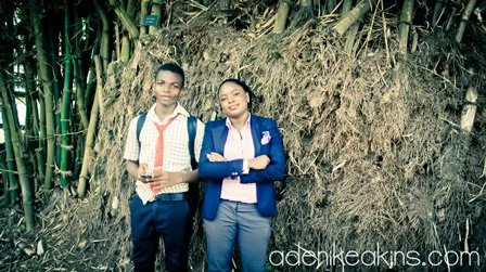A boy and girl standing together outdoors near a slope with tall grass and bamboo, smiling for the photo.