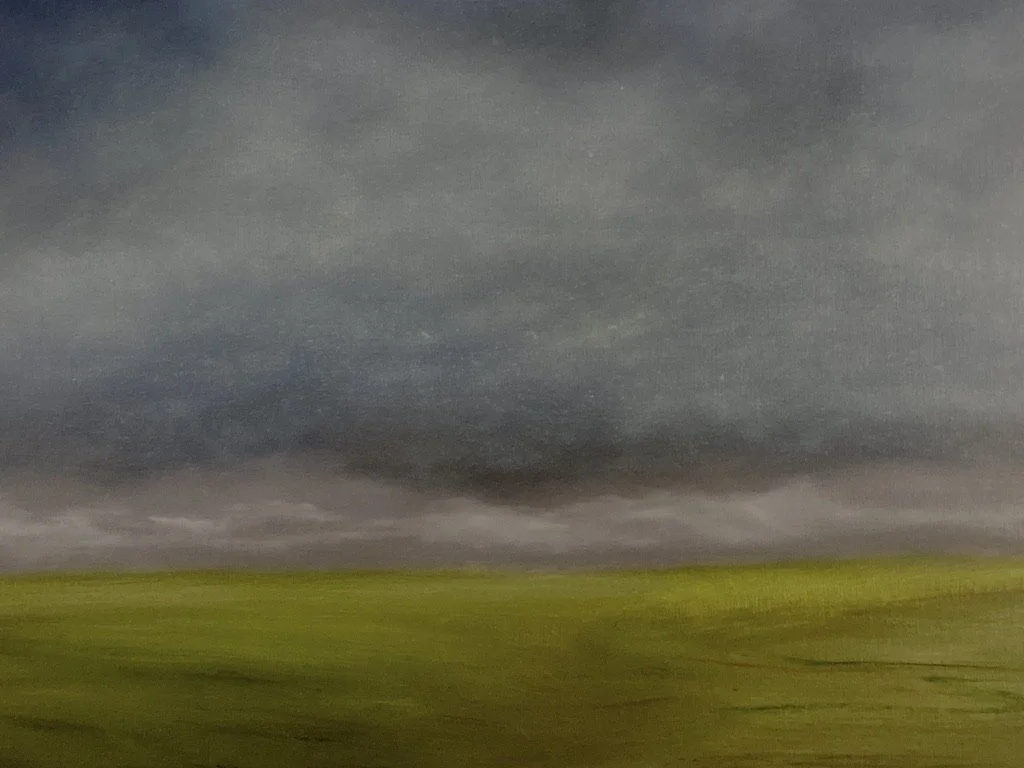 A dramatic stormy sky over a vast green field.