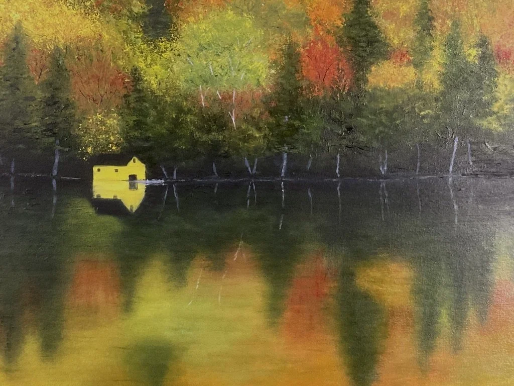 A yellow boat house and fall foliage on a lake with colorful reflections in the water.