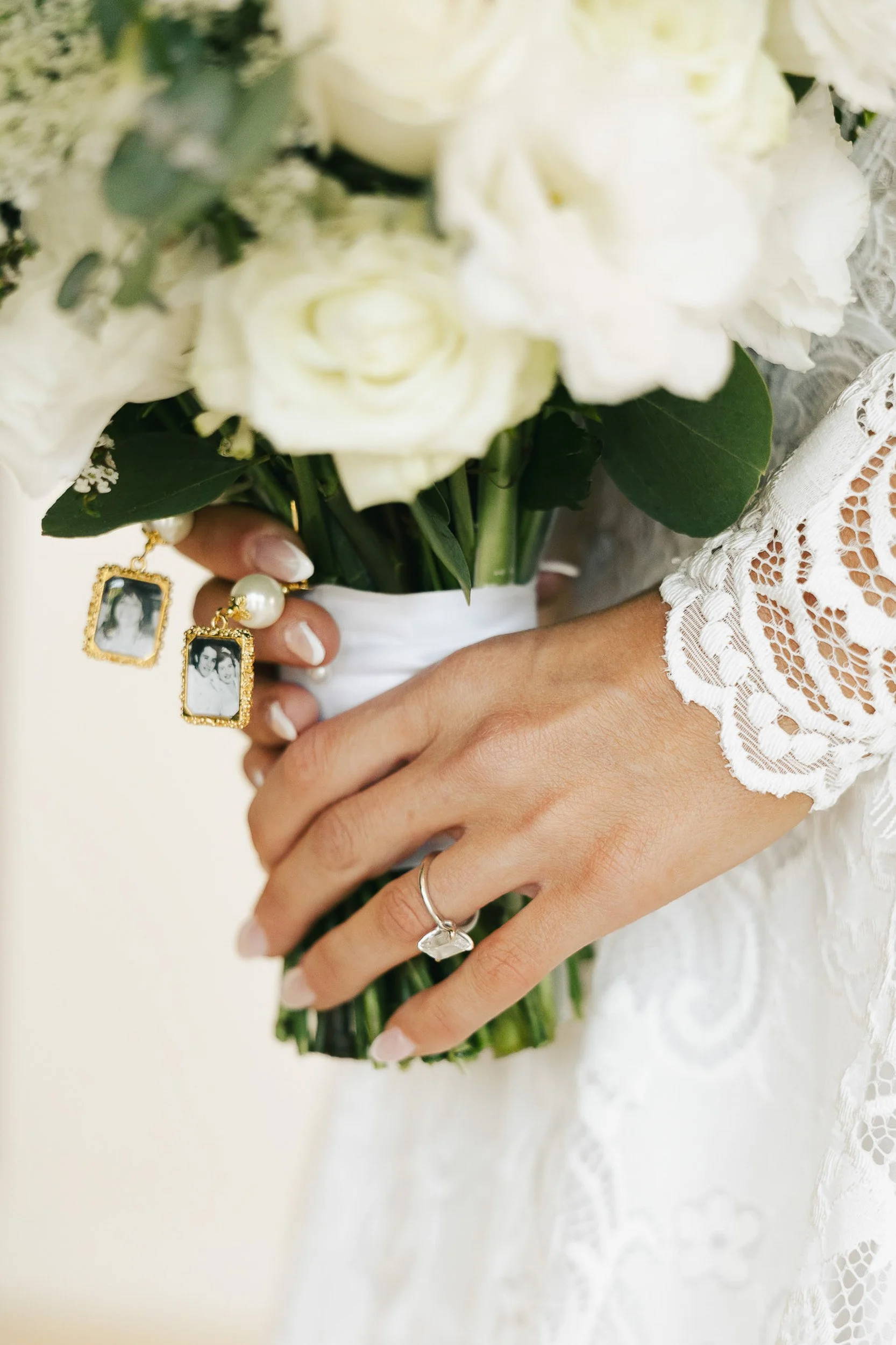 Person holding a bouquet of white flowers, wearing a lace dress, with jewelry including earrings, rings, and a bracelet.