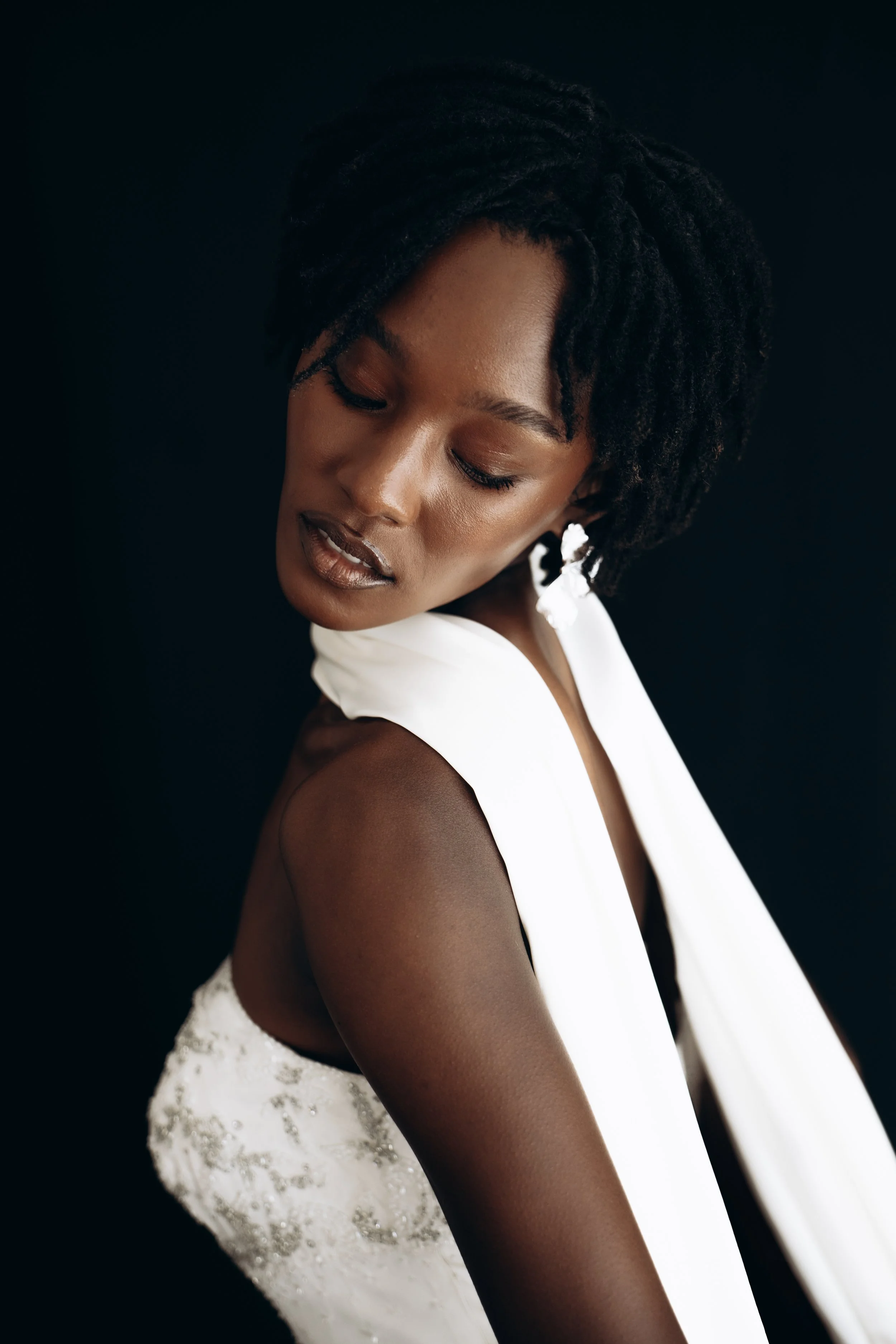 A bride with a neck scarf posing in front of a black background with her eyes closed.