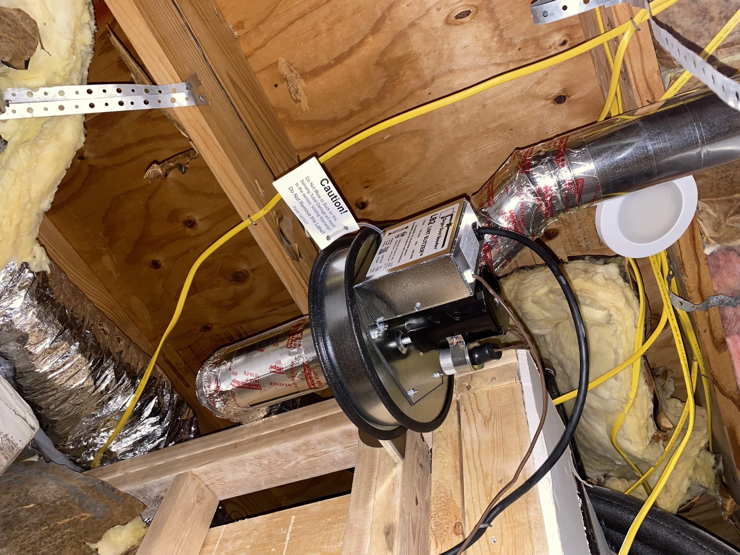 View of a construction or renovation space with wood framing, yellow electrical wires, insulation, and ductwork, including a metal fan motor and caution signs.