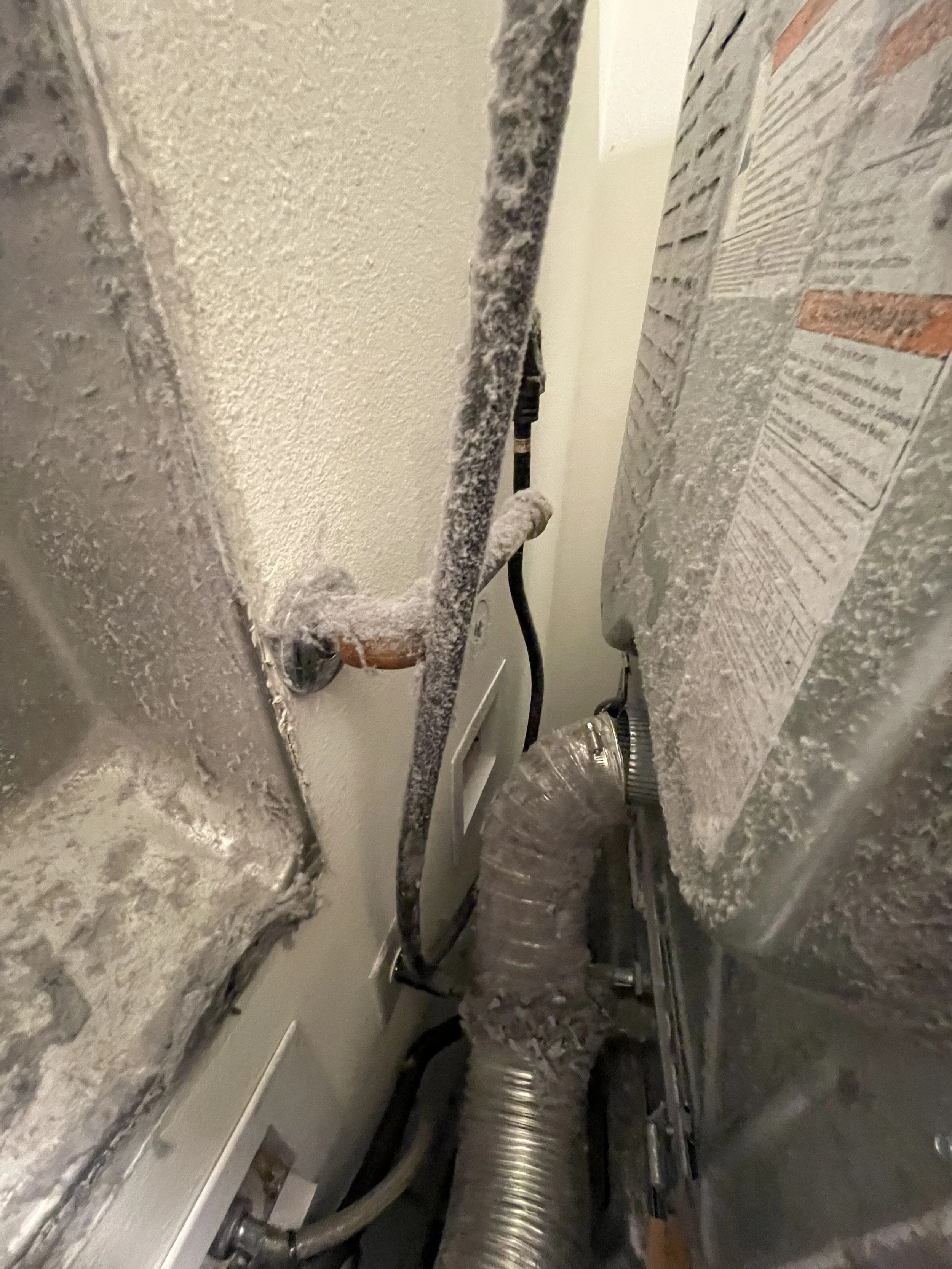 Close-up view of an electrical area showing insulation covered wires, a flexible metallic duct, and some electrical components on the wall.