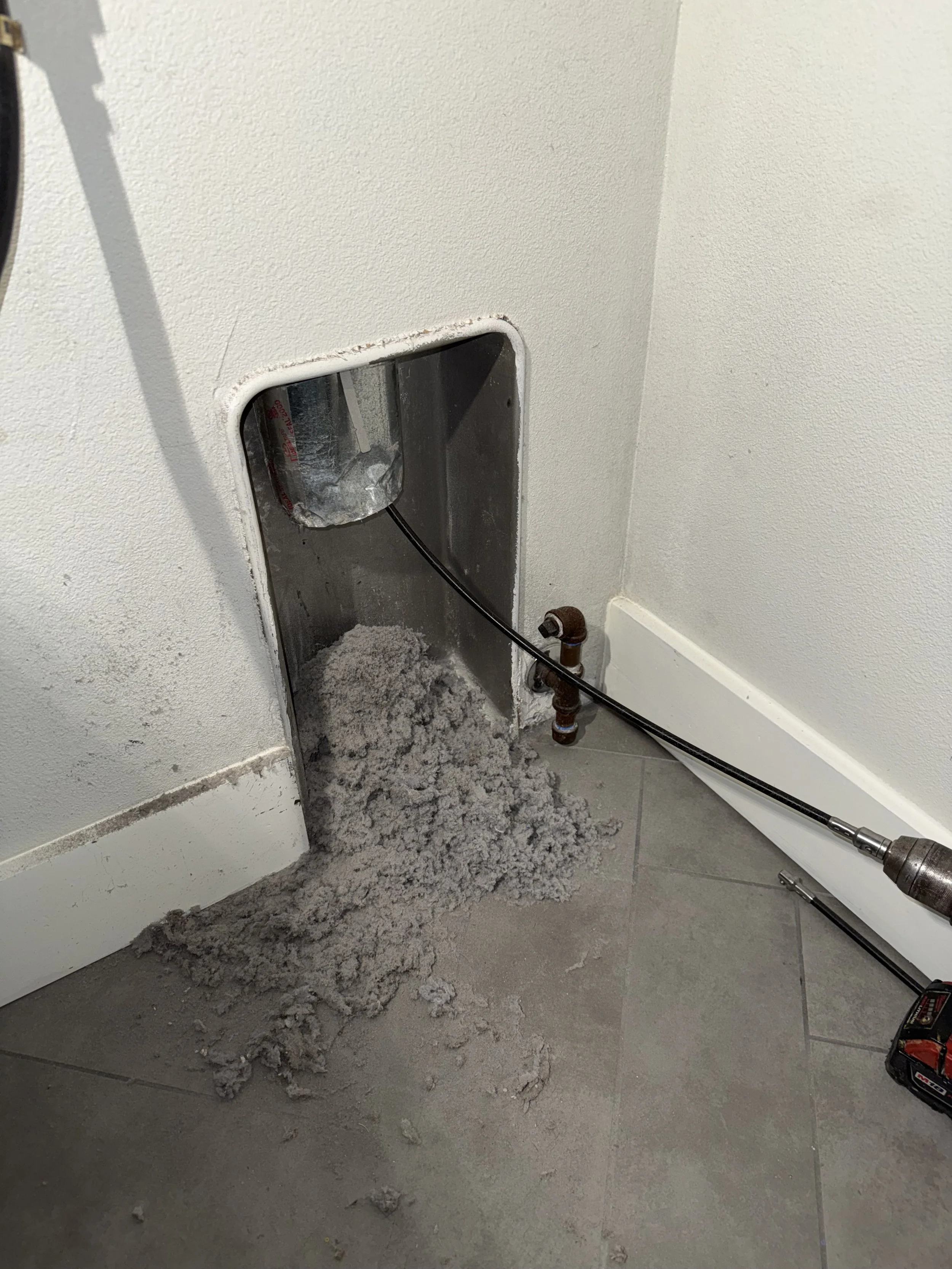 Floor with debris and dust, a removed appliance hatch, and tools nearby in a room under repair.