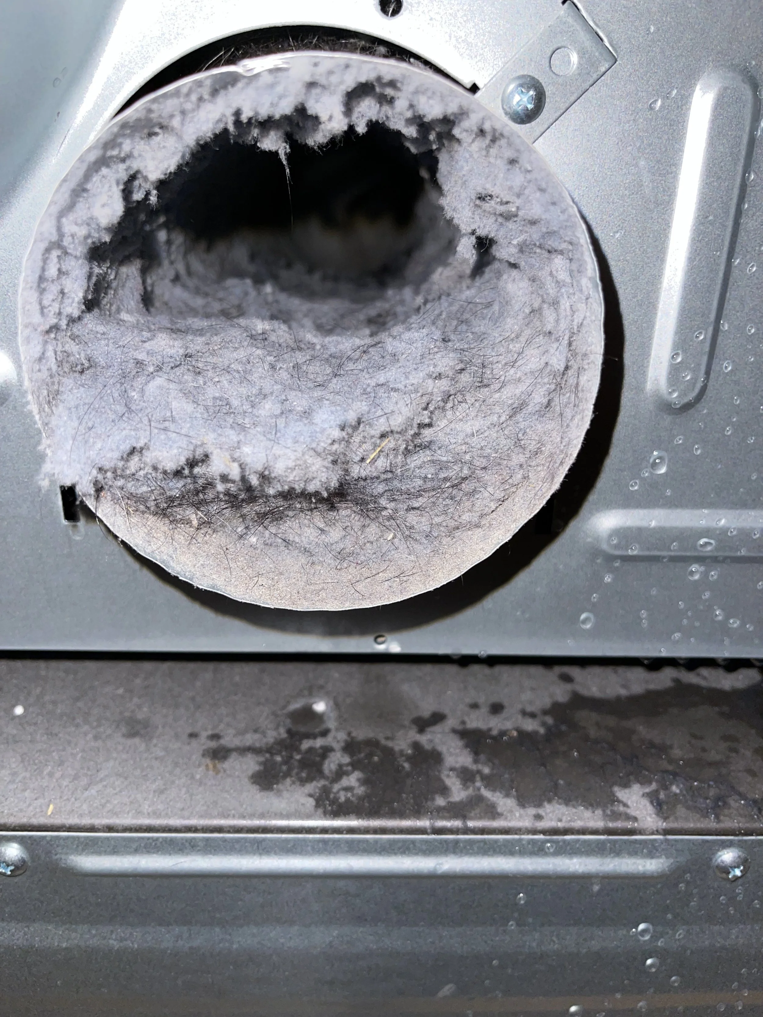 A close-up of a dryer vent with a buildup of lint inside the opening.