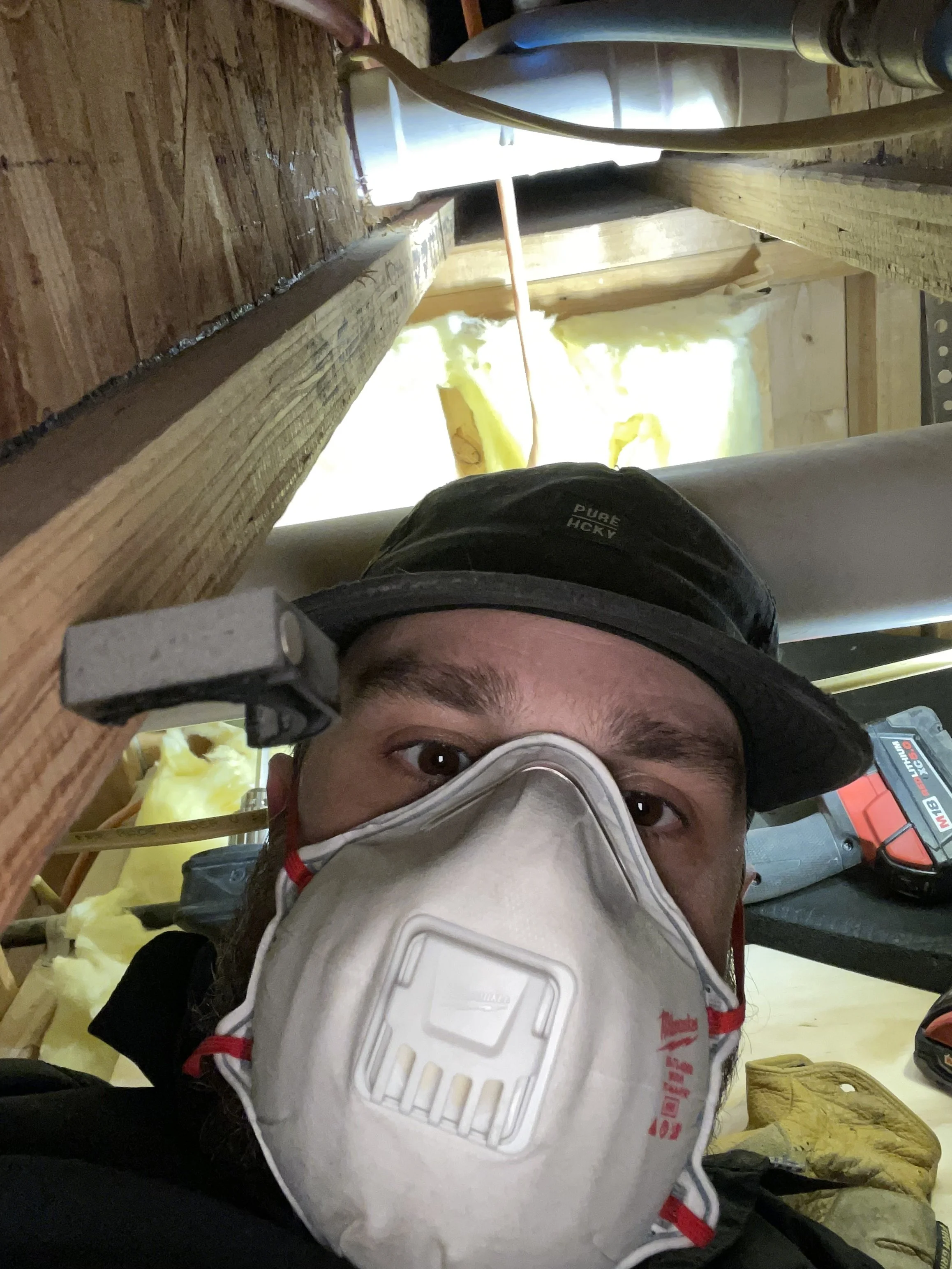 A person wearing a white mask and helmet viewed from below, with construction materials and tools around in a workshop or construction site.