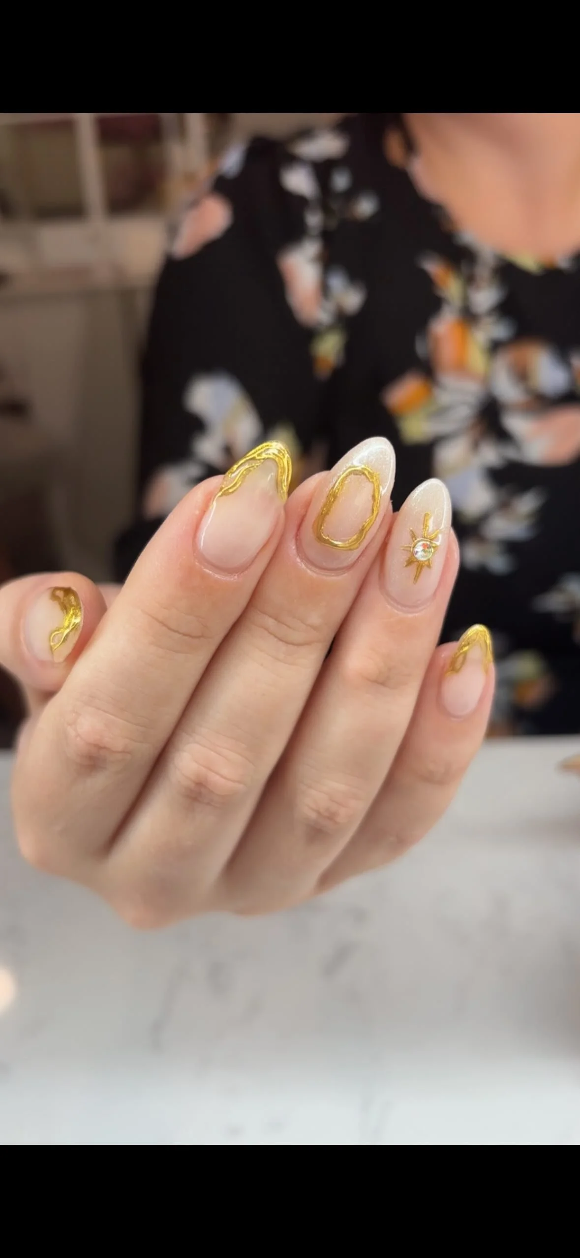 Close-up of a person's hand with decorated nails featuring gold accents and a small star-shaped charm with a gemstone on one nail.