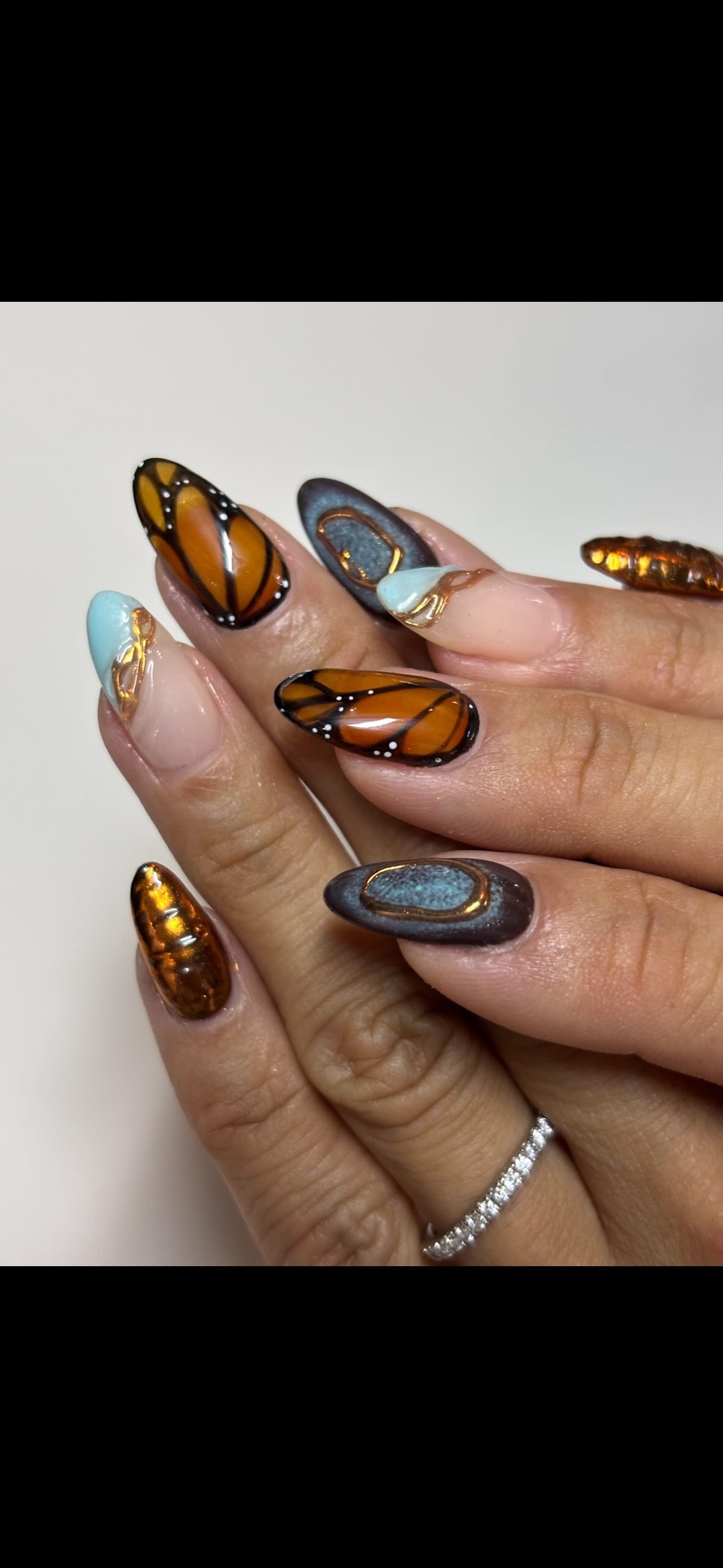 Close-up of manicured nails painted with butterfly and abstract designs in black, orange, blue, and metallic colors.