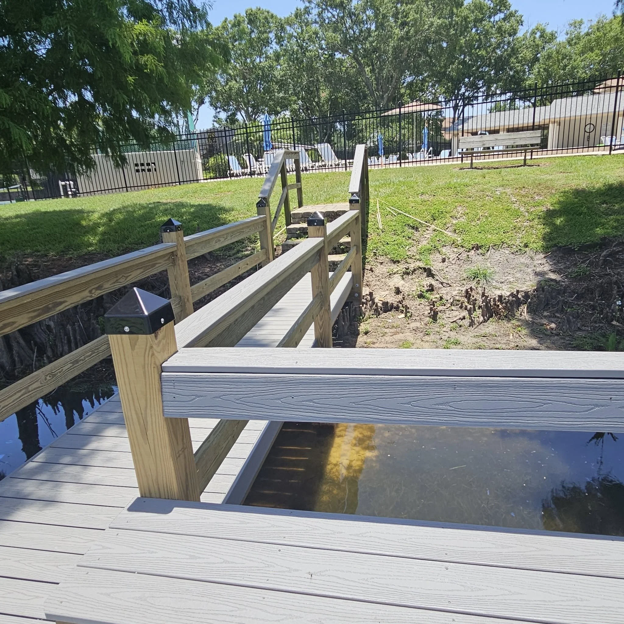 A wooden ramp leading to a grassy area beside a pond.