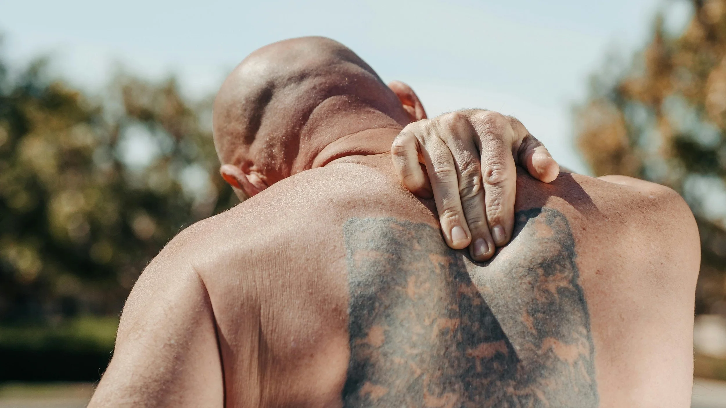 Tattooed man holding his shoulder in discomfort outdoors highlighting the importance of injury prevention in a personalized training program. Photo by Kindel Media on Pexels