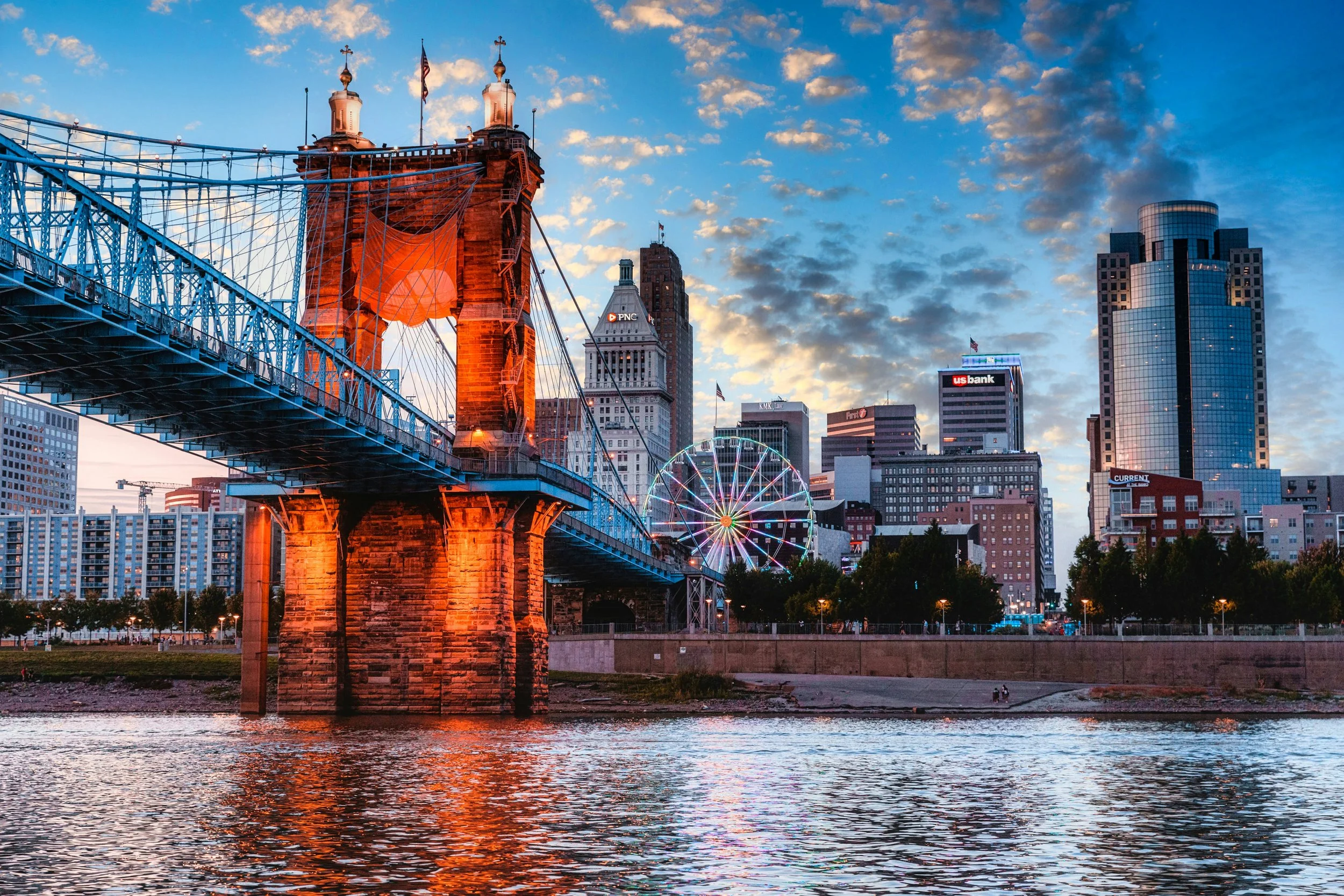 Sunset over Cincinnati skyline with a bridge in the foreground and a Ferris wheel in the background.