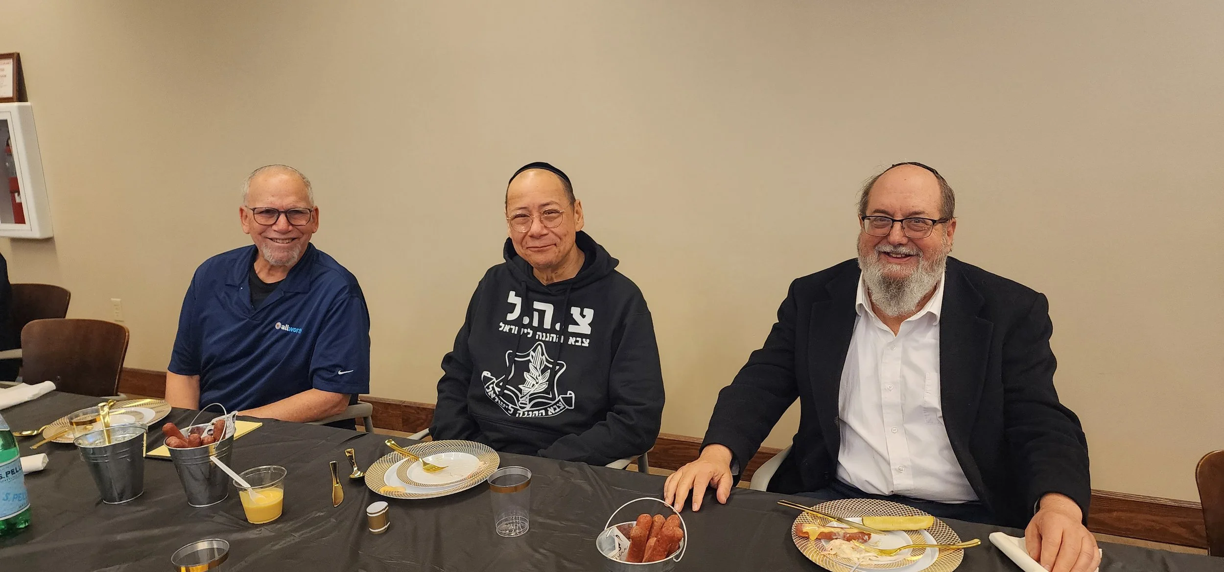 Three men sitting at a banquet table with food and drinks, smiling at the camera.