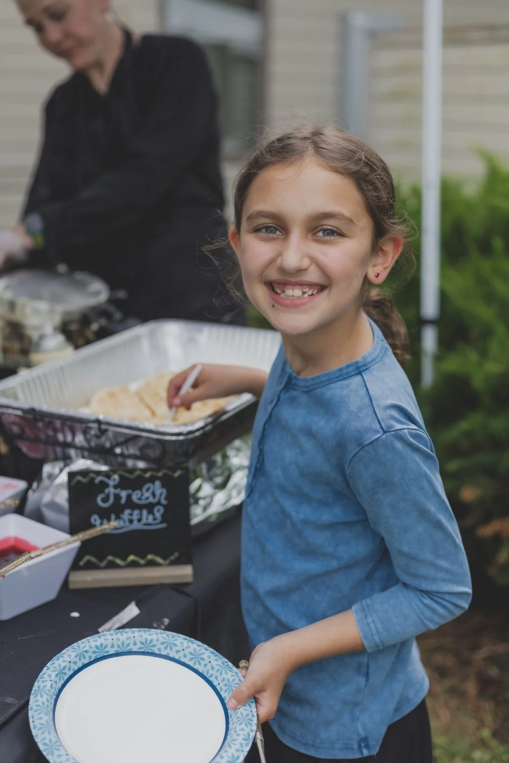 Smiling girl with blue shirt holding a decorative plate at a food stand with a sign that says "Fresh Cookies".