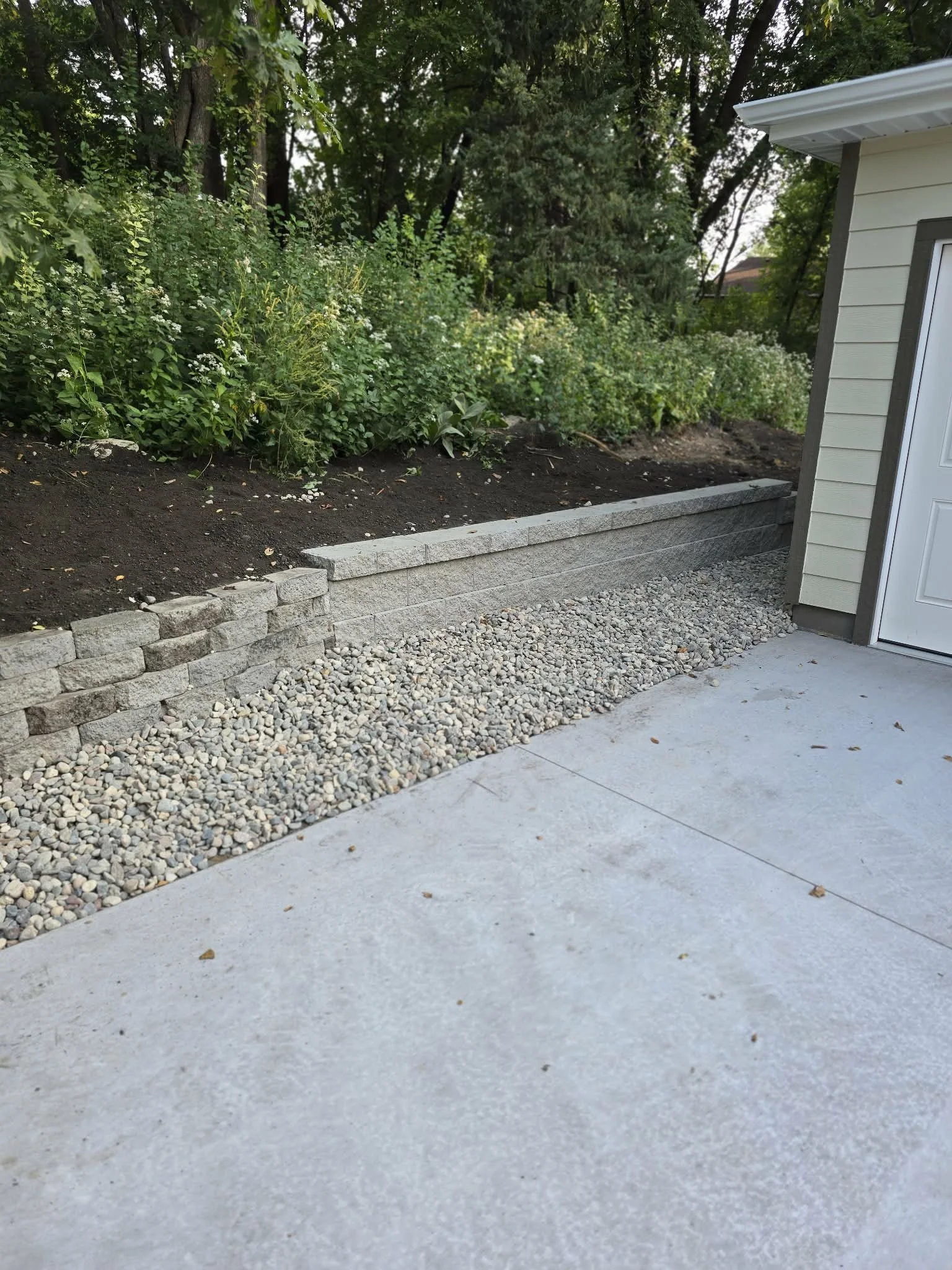 retaining wall with gravel drainage edge and concrete patio transition