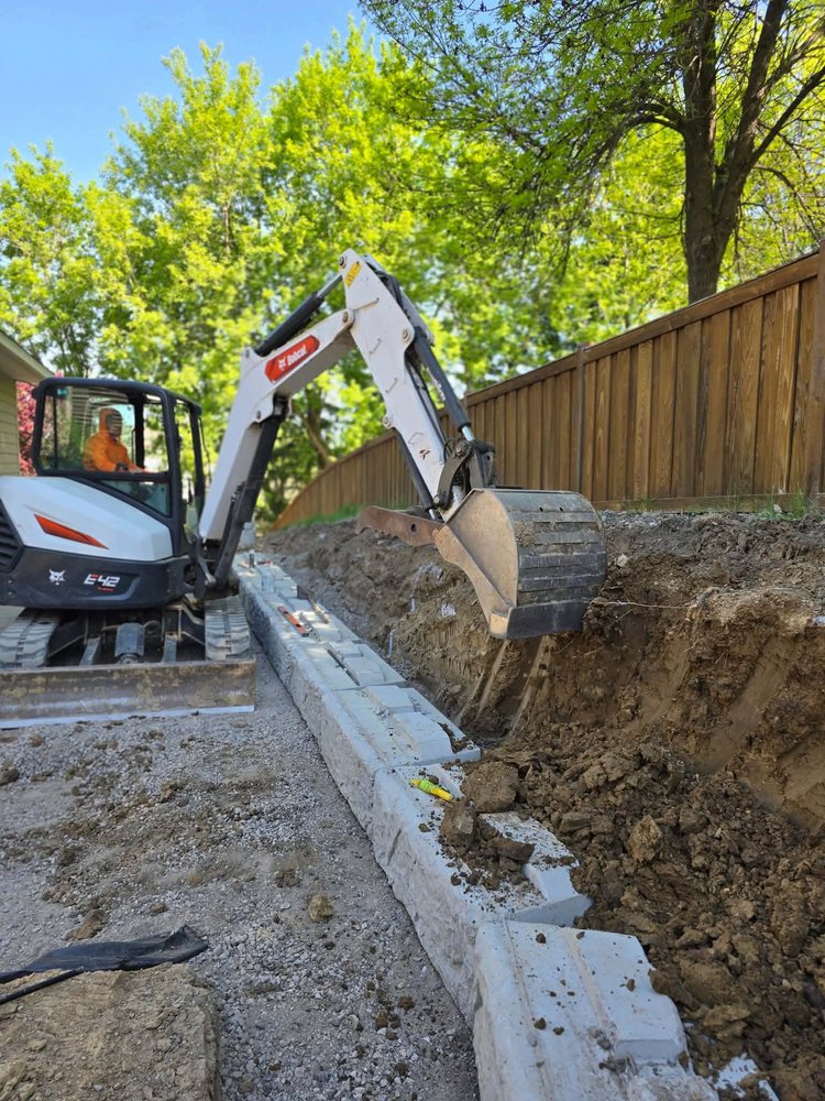Excavator preparing the foundation and drainage area for a structural retaining wall installation