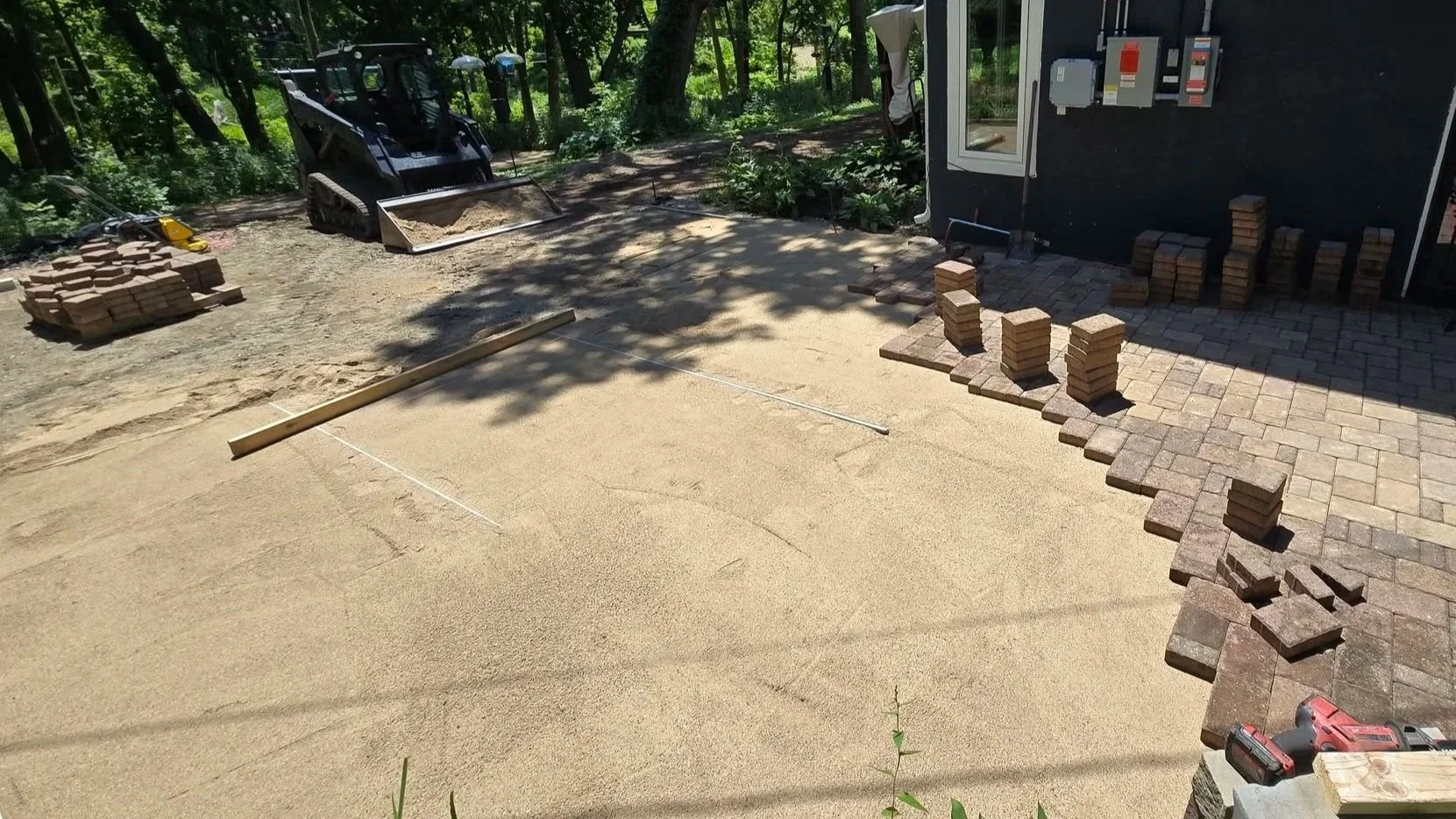 Paver patio installation in progress showing prepared bedding material, screed rails and partially installed pavers