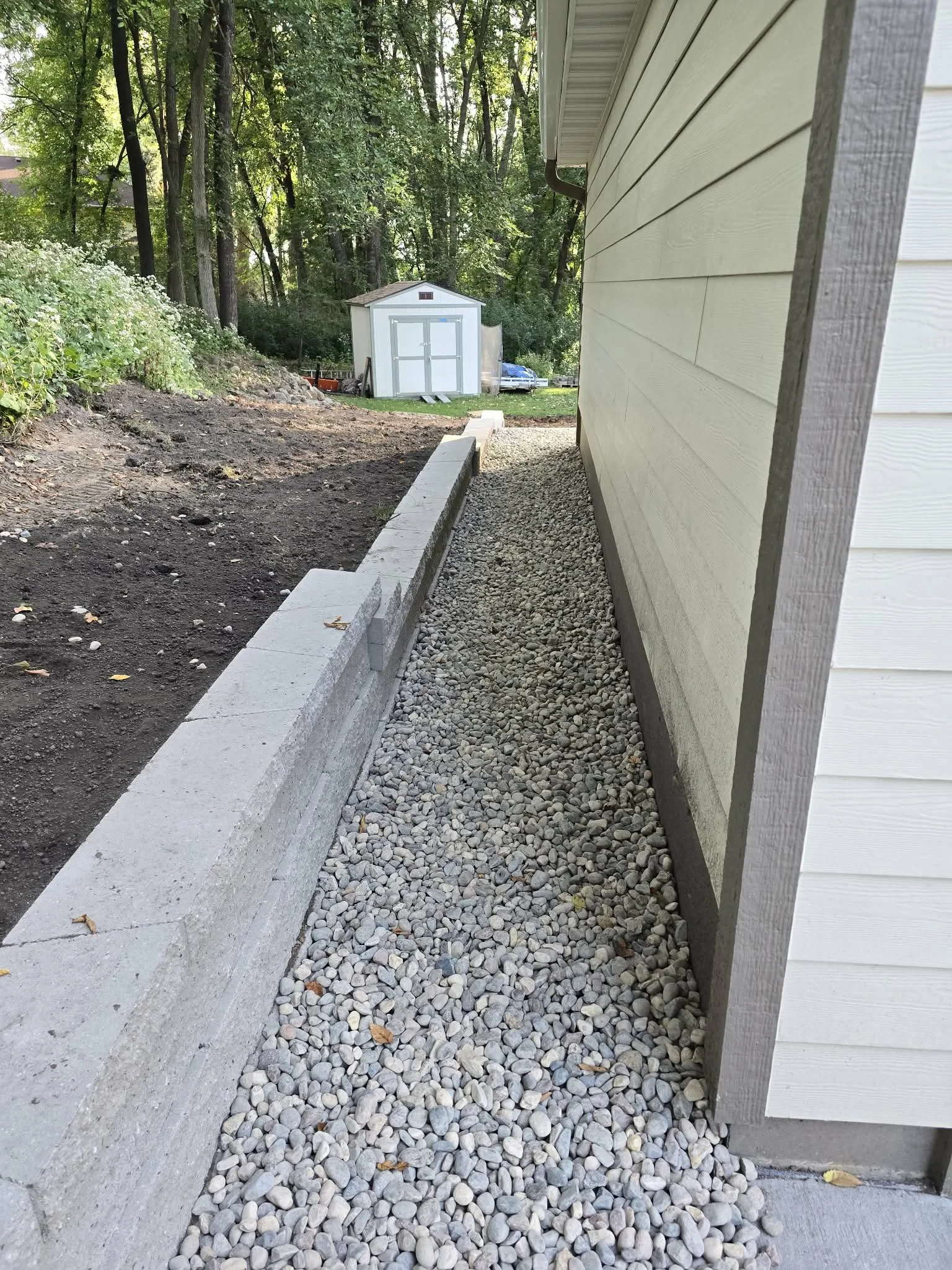 narrow retaining wall with drainage rock side yard installation for garage protection 