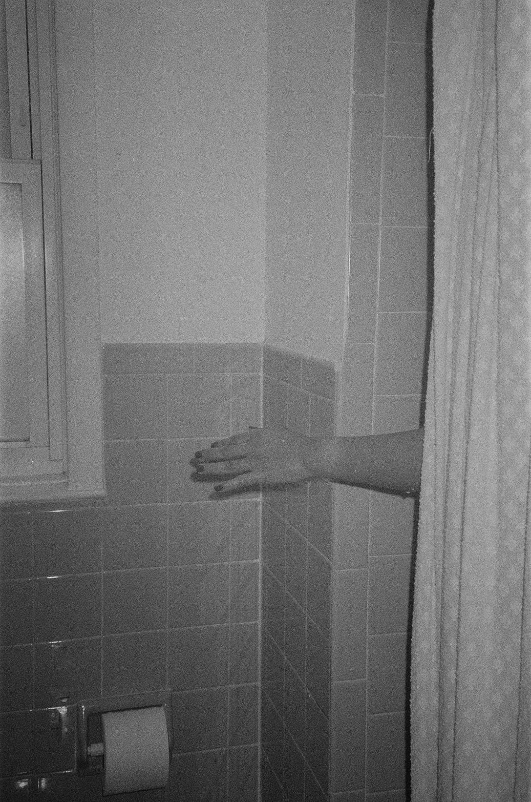 Black and white photo of a bathroom with a hand reaching out from behind a wall.