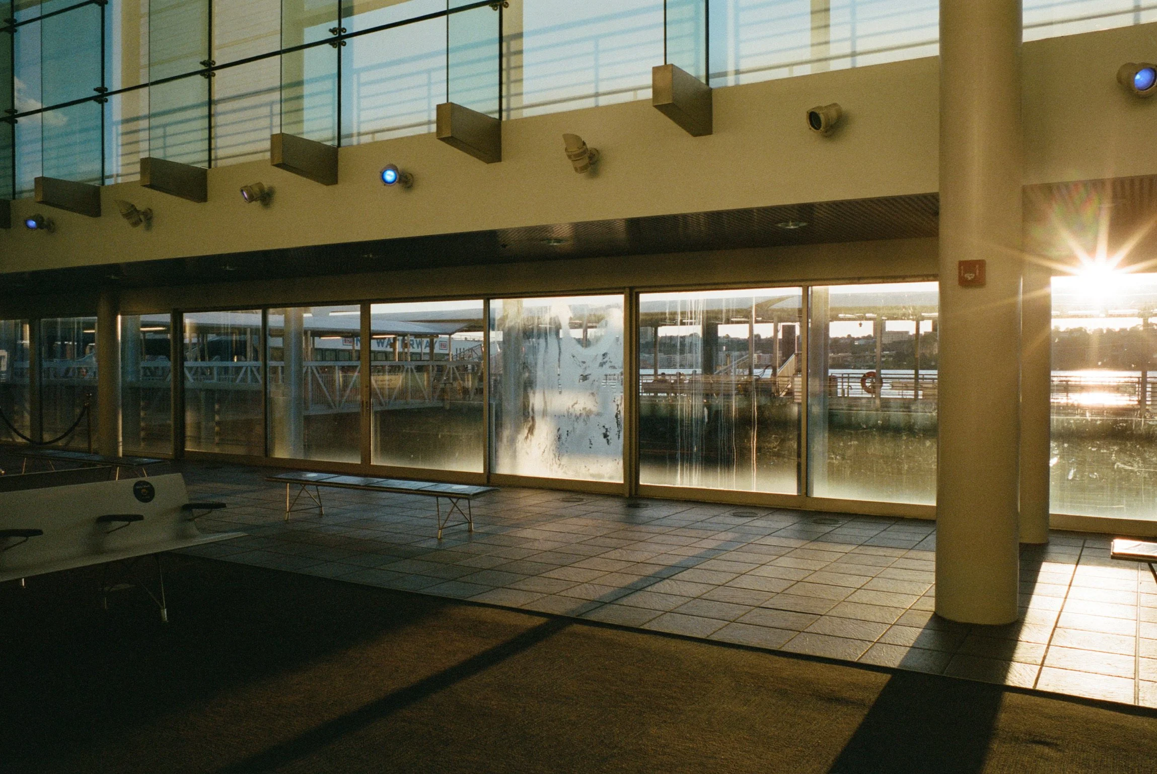 Indoor scene of an airport terminal with large glass windows, benches, and sunlight shining through, creating reflections and shadows.