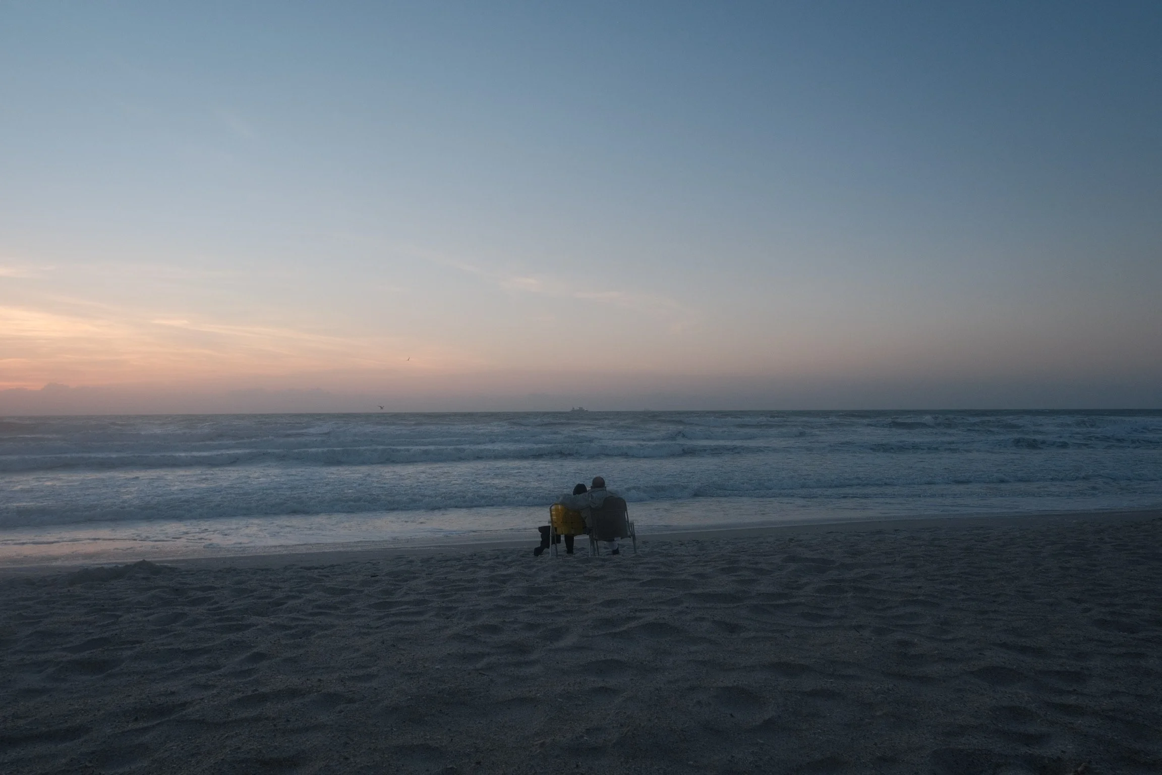Two people sitting on chairs on the beach near the ocean at sunset.