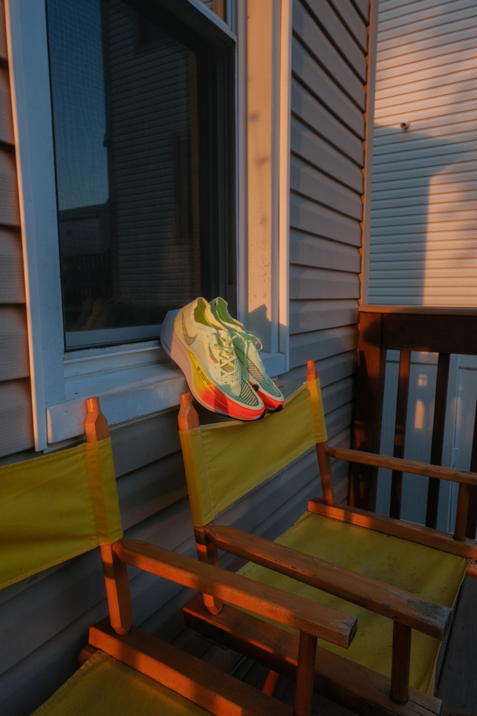 A pair of running shoes resting on a balcony window ledge, with two yellow chairs in the foreground and the sunlight casting warm glow.