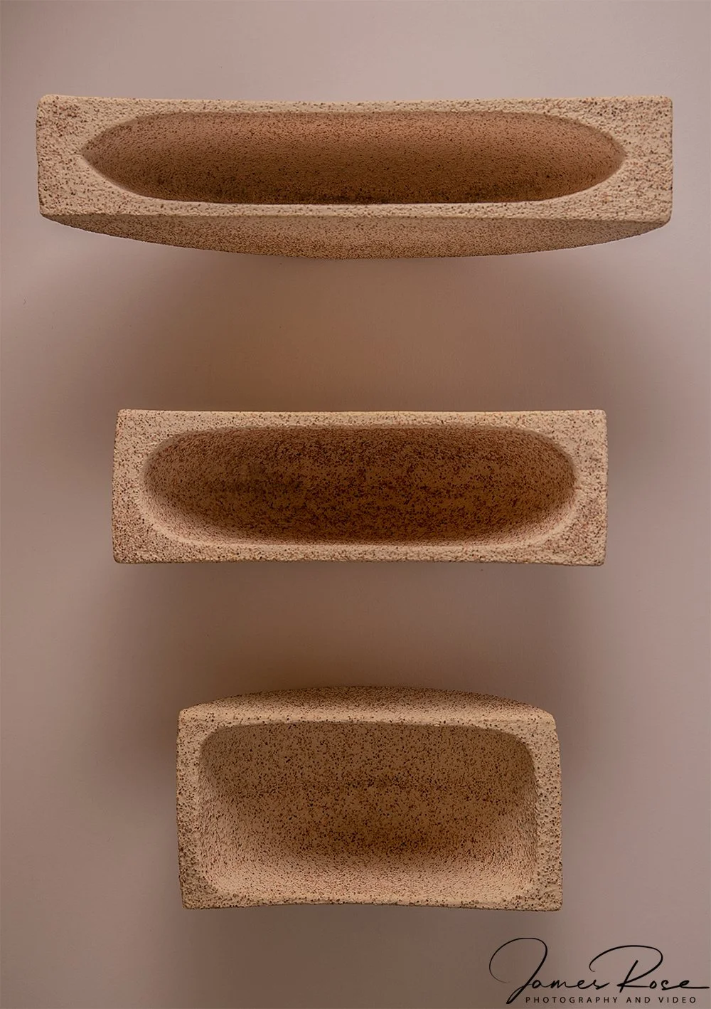 Three rectangular, textured stone planters stacked vertically, each with a smooth, rounded interior hollow.
