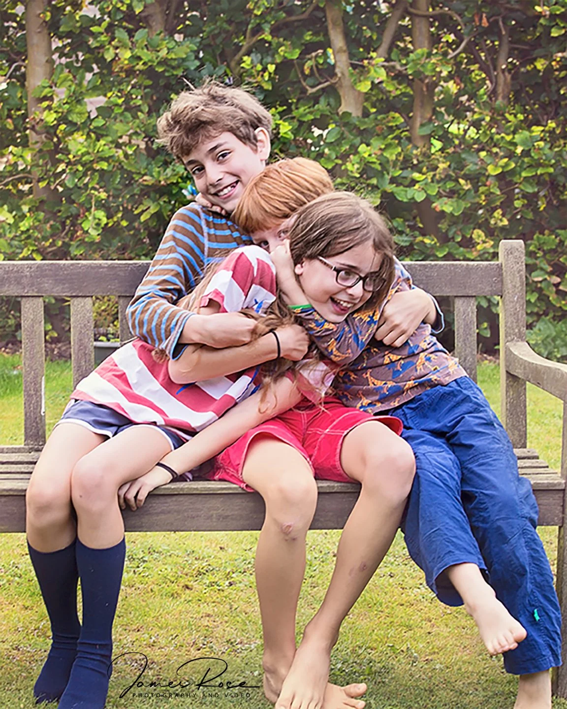 Three children sitting on a wooden park bench, playing and laughing together.