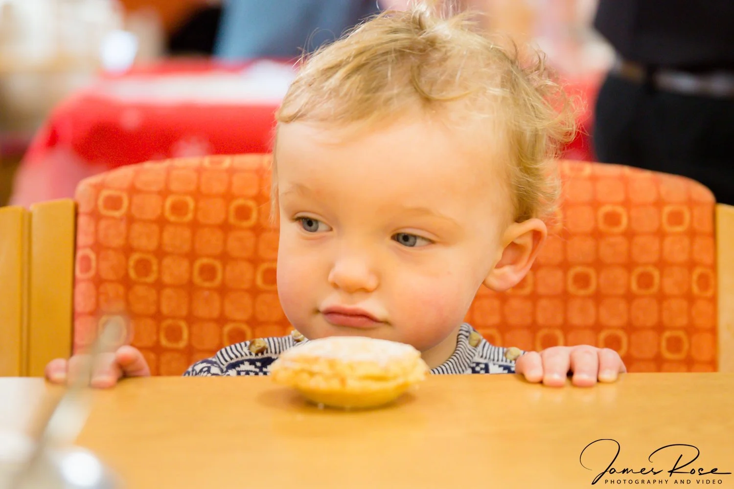 Young child with light skin and curly blonde hair sitting at a table, looking at a donut on a plate in front of him.