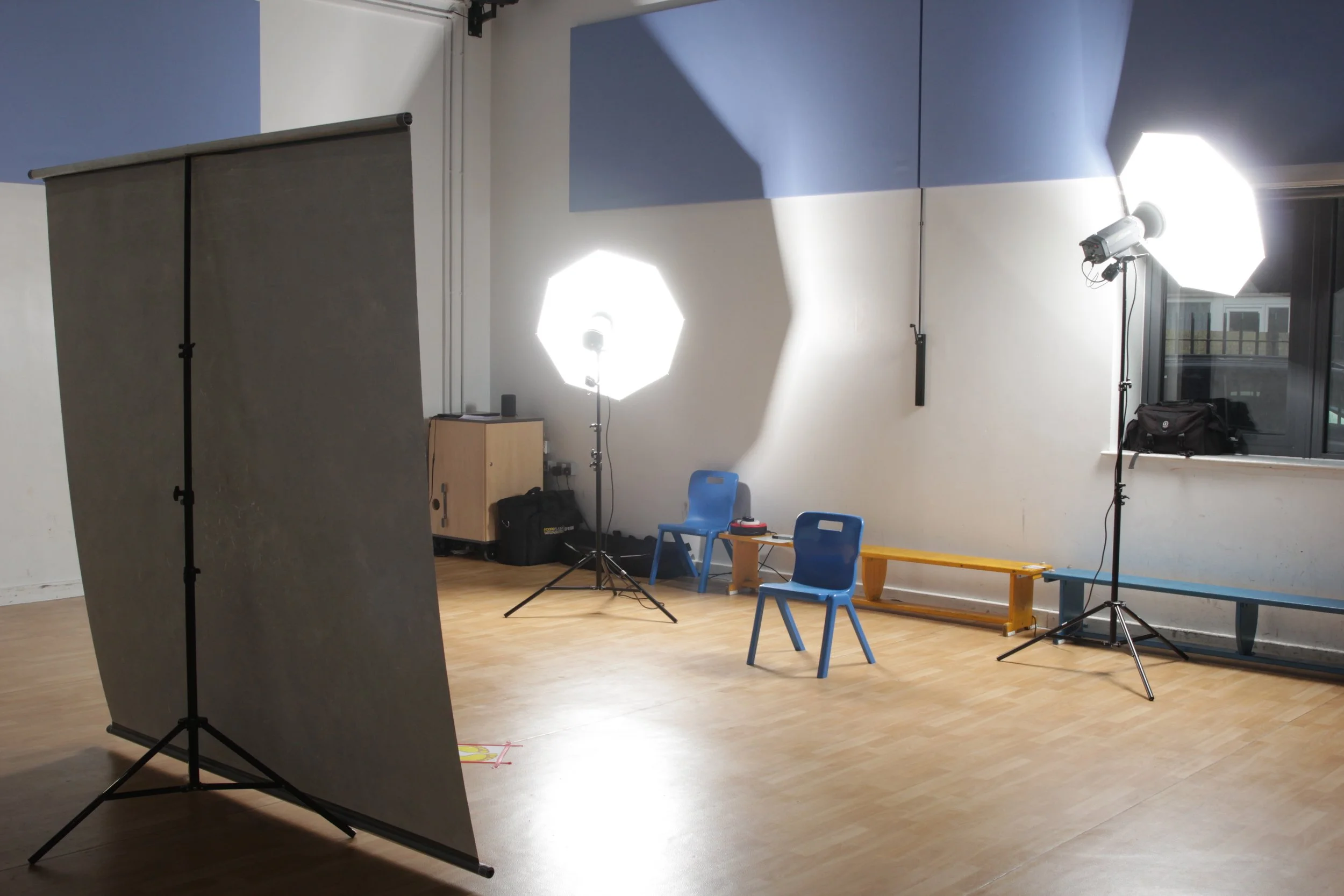 Photo of a photography studio with professional lighting, blue chairs, a closet, and a window.