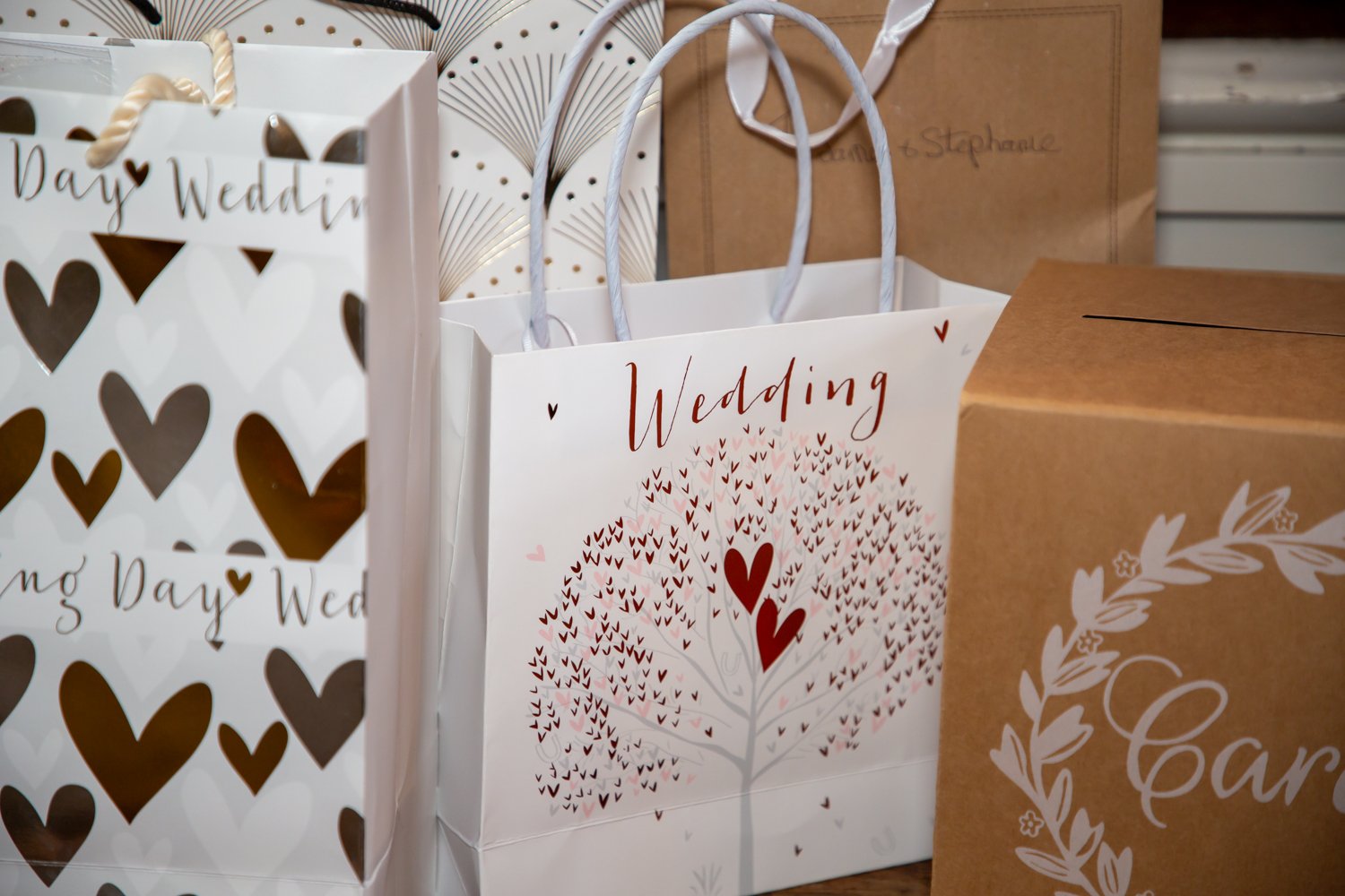 Multiple gift bags with wedding-themed designs, including hearts and wedding phrases, on a table.