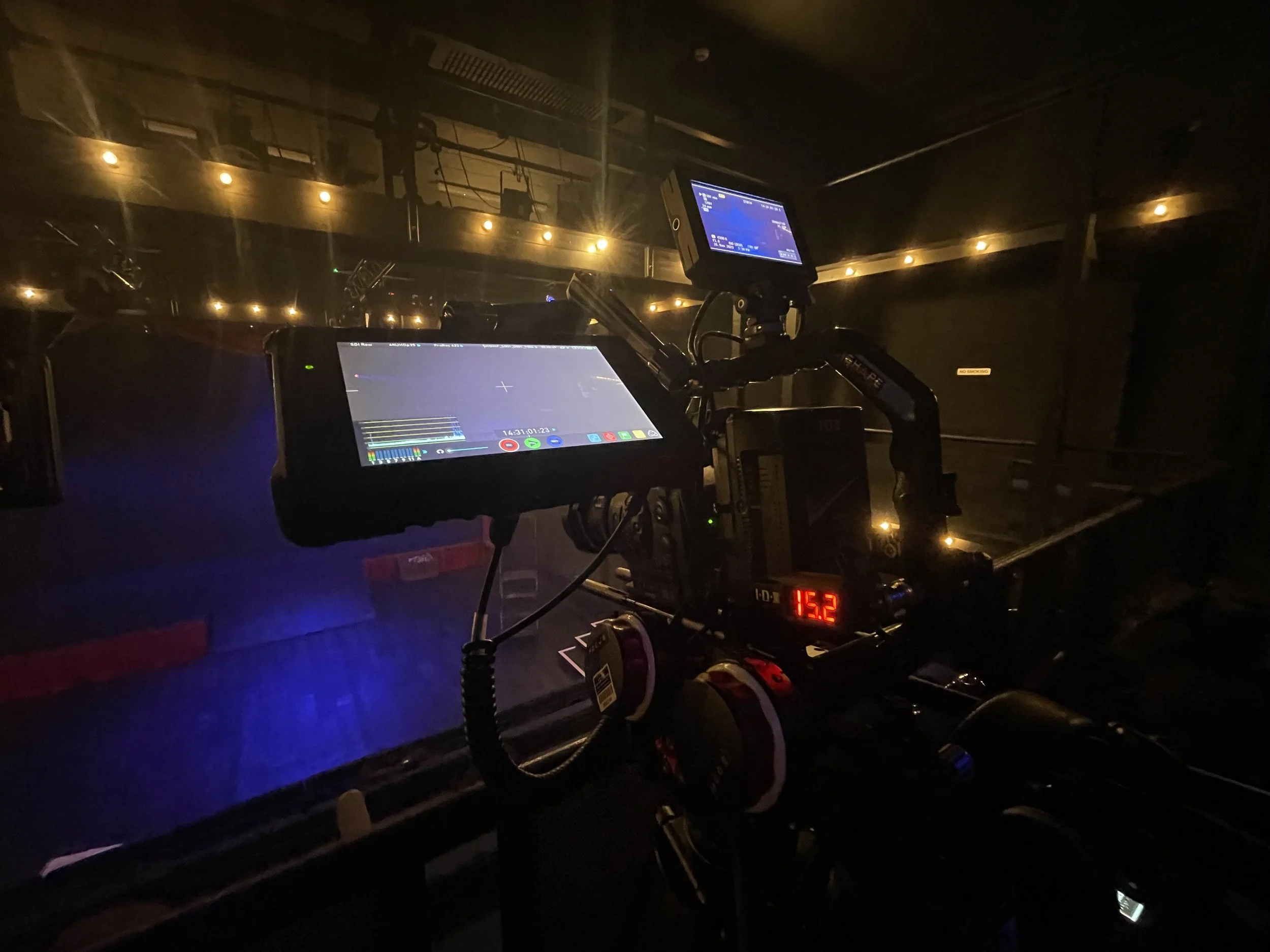Film or photography camera setup in a dimly lit environment, with multiple screens and equipment, possibly on a stage or set.