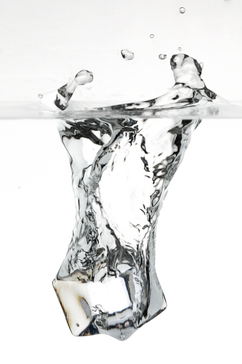 Ice cube splashing into water with bubbles and ripples.