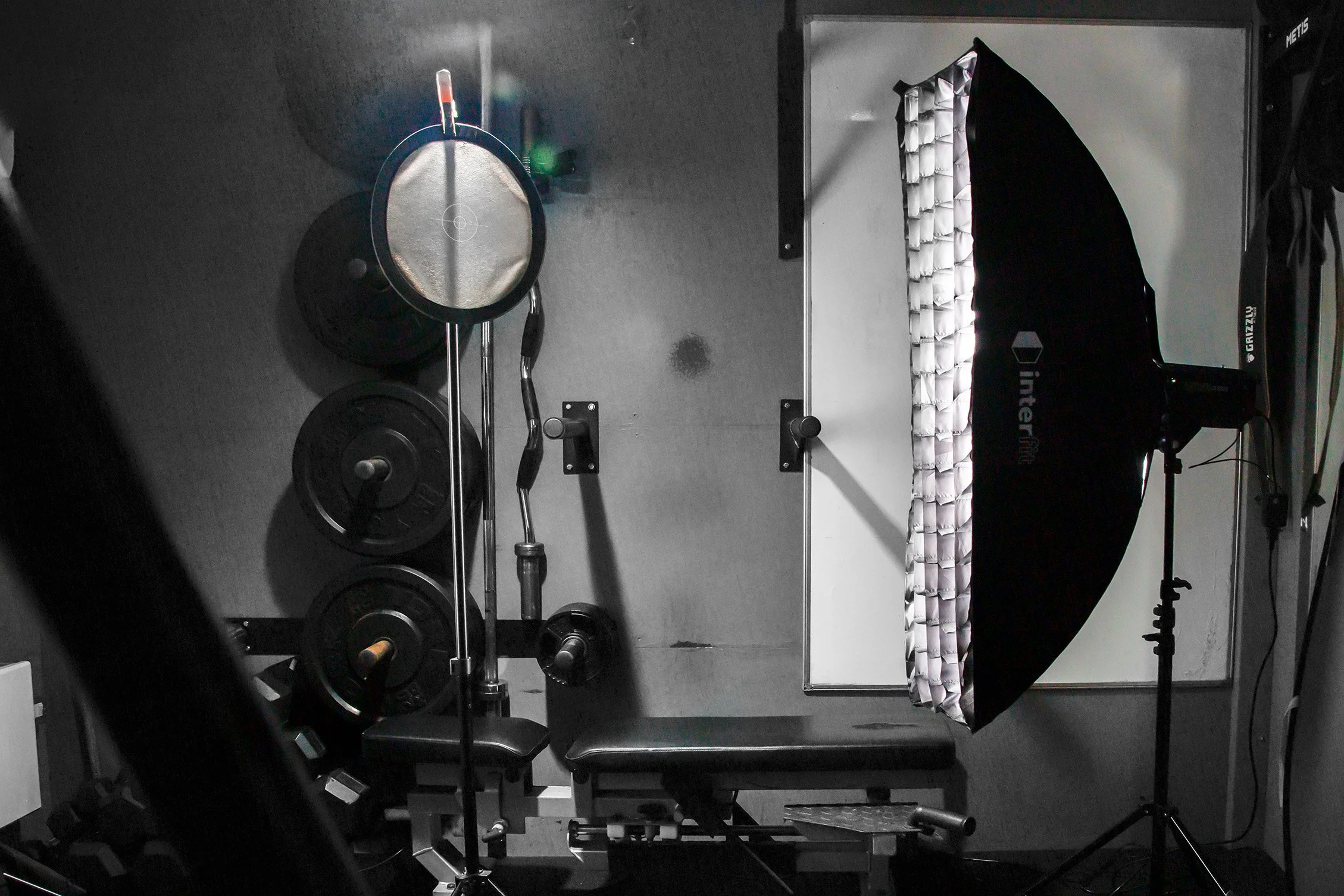 Photography studio setup with softbox lighting, a white backdrop, and weight plates stacked on a stand.