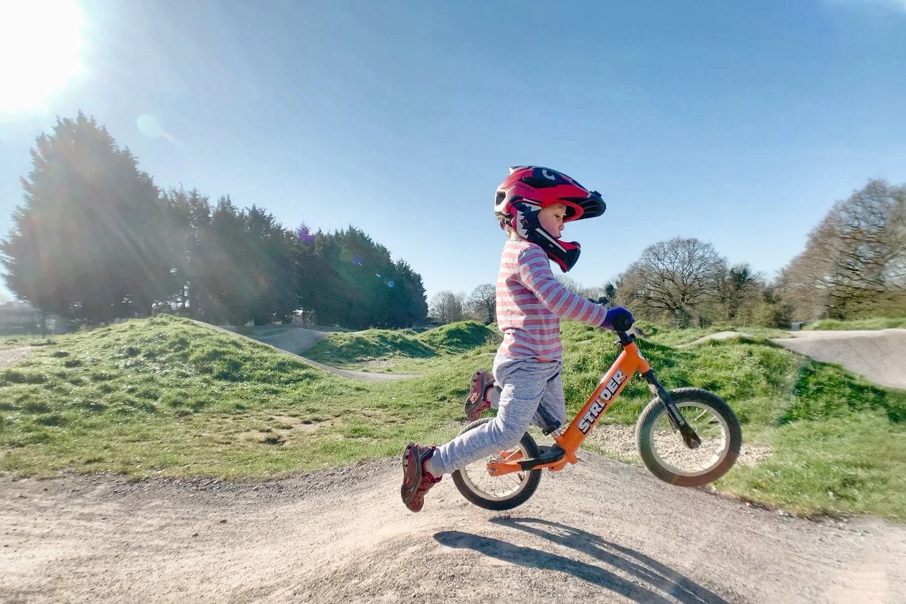 Child wearing helmet riding a balance bike on outdoor dirt trail on sunny day